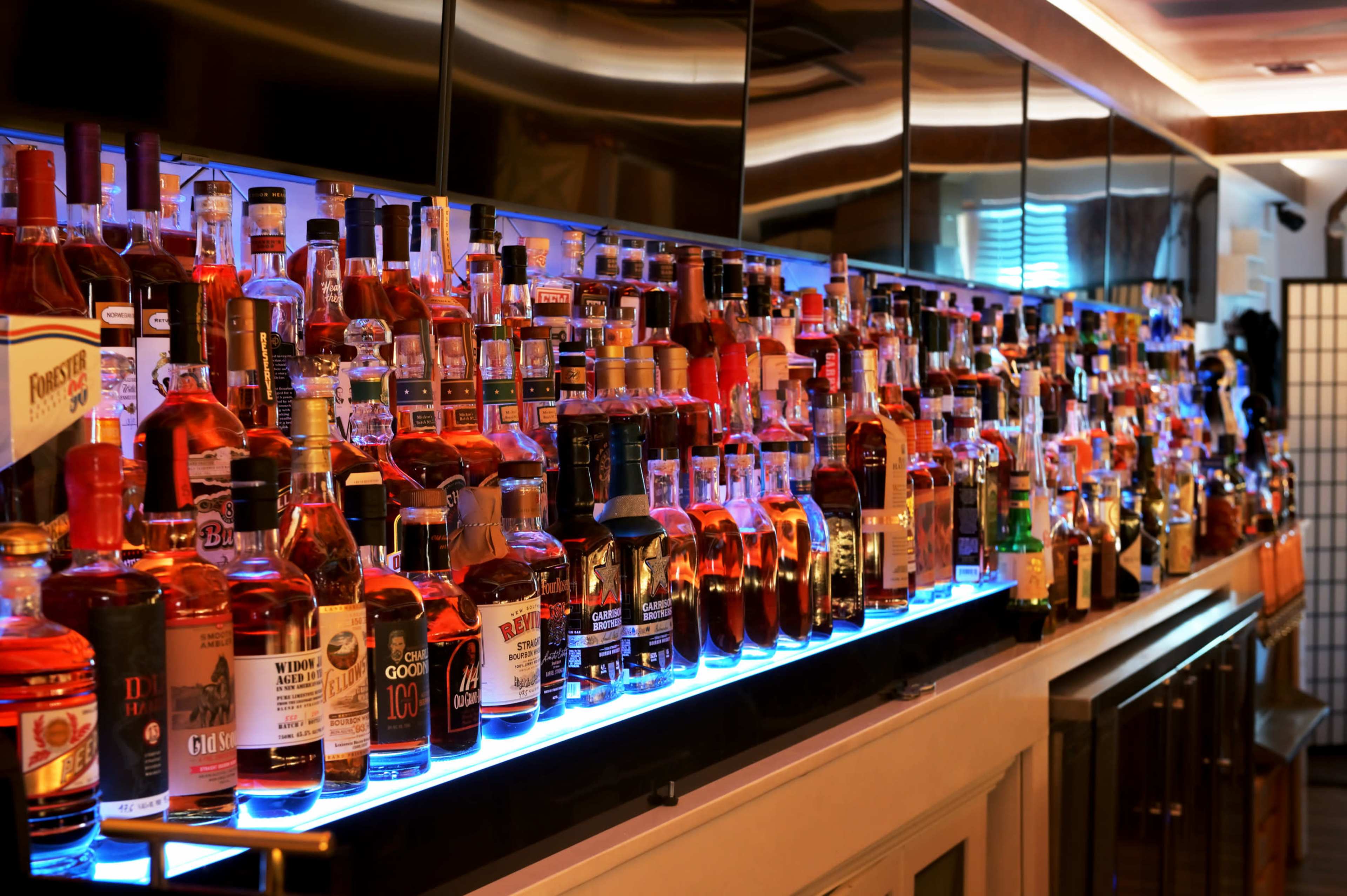 A brightly lit bar displays a wide array of liquor bottles arranged neatly on shelves.