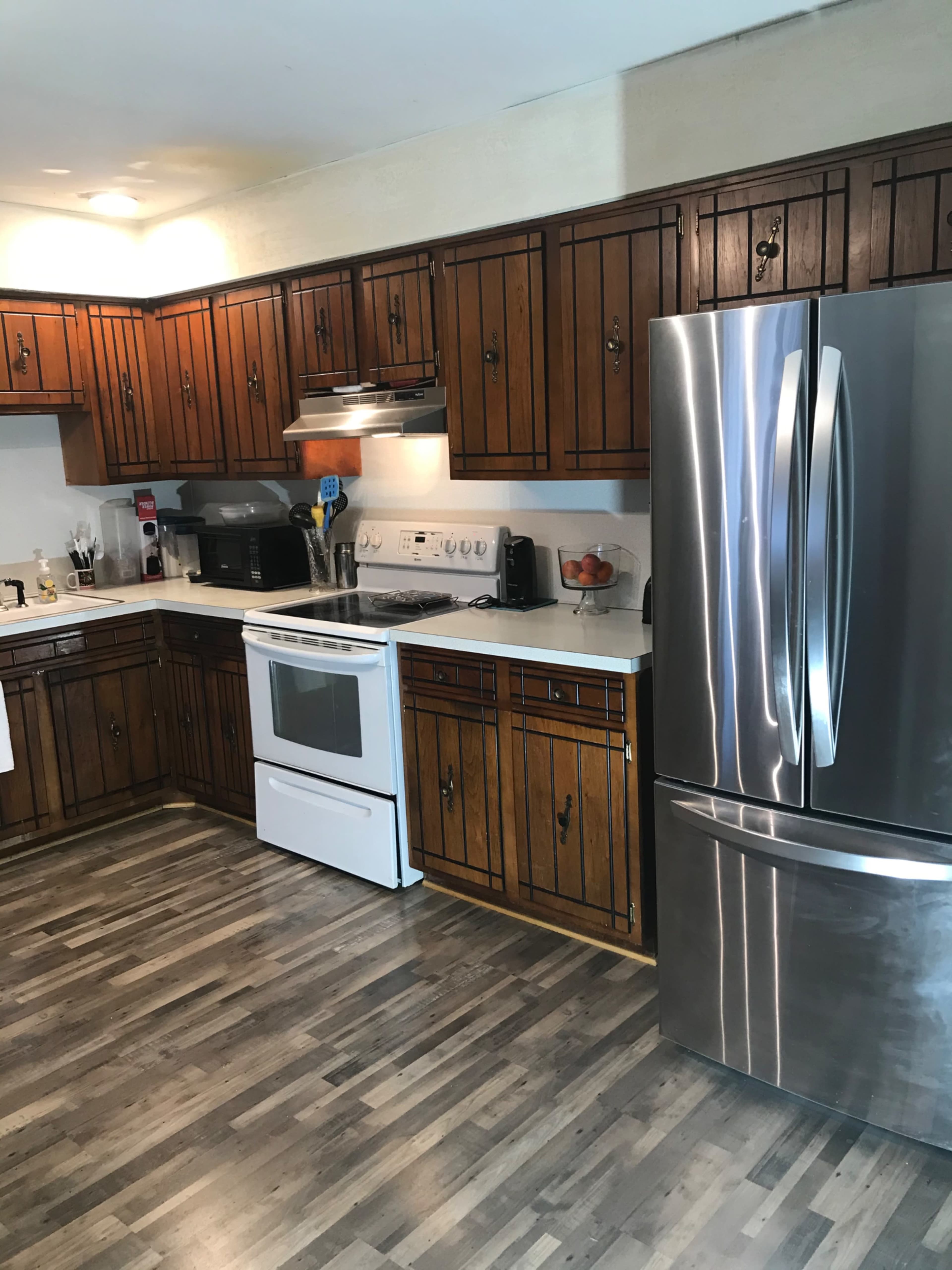 A kitchen with wooden cabinets, a stainless steel refrigerator, a white oven, and a countertop with various kitchen appliances.