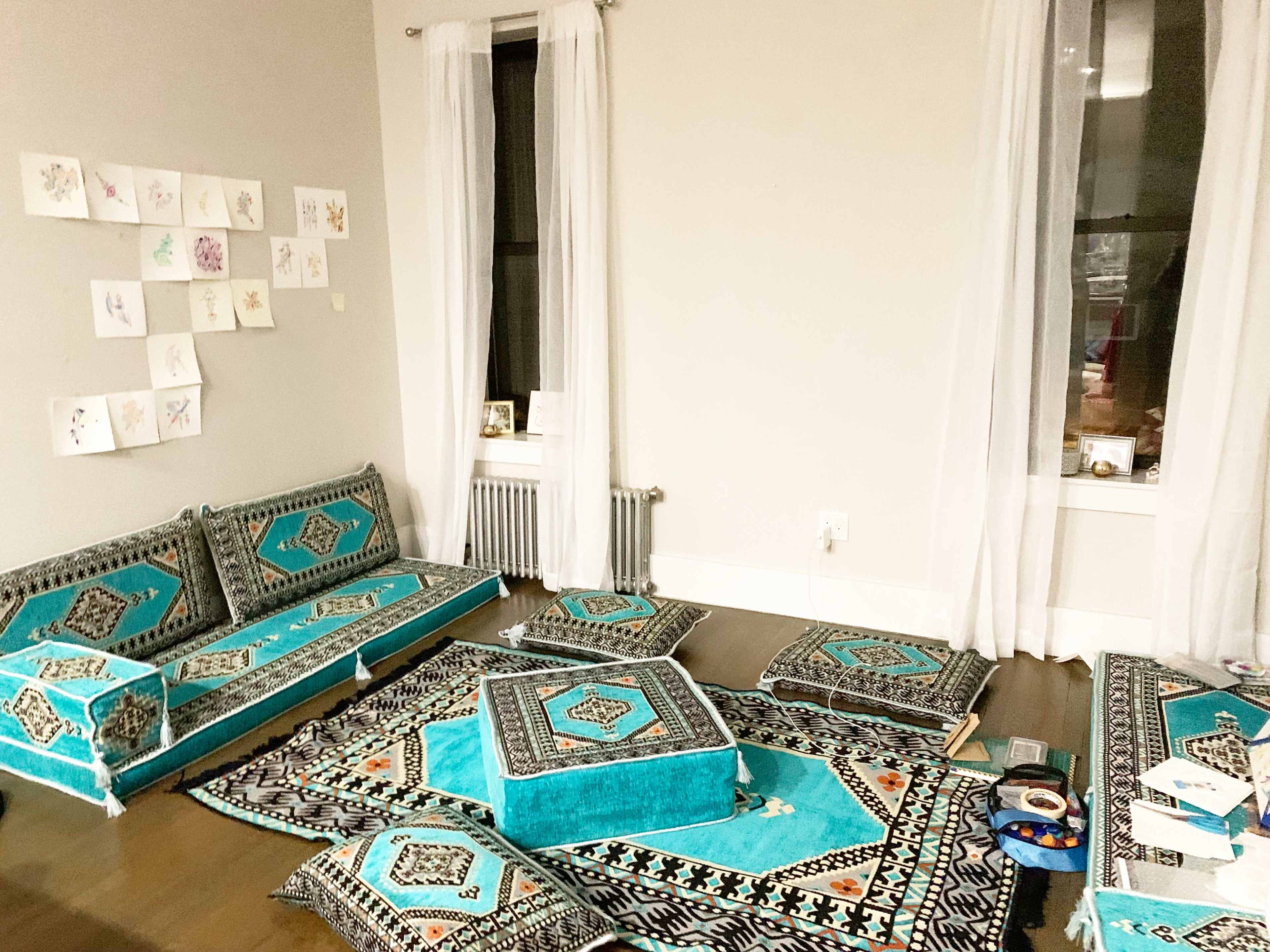 The room features a patterned carpet and cushions in turquoise and black, with a sofa against one wall and artwork hanging on the other.