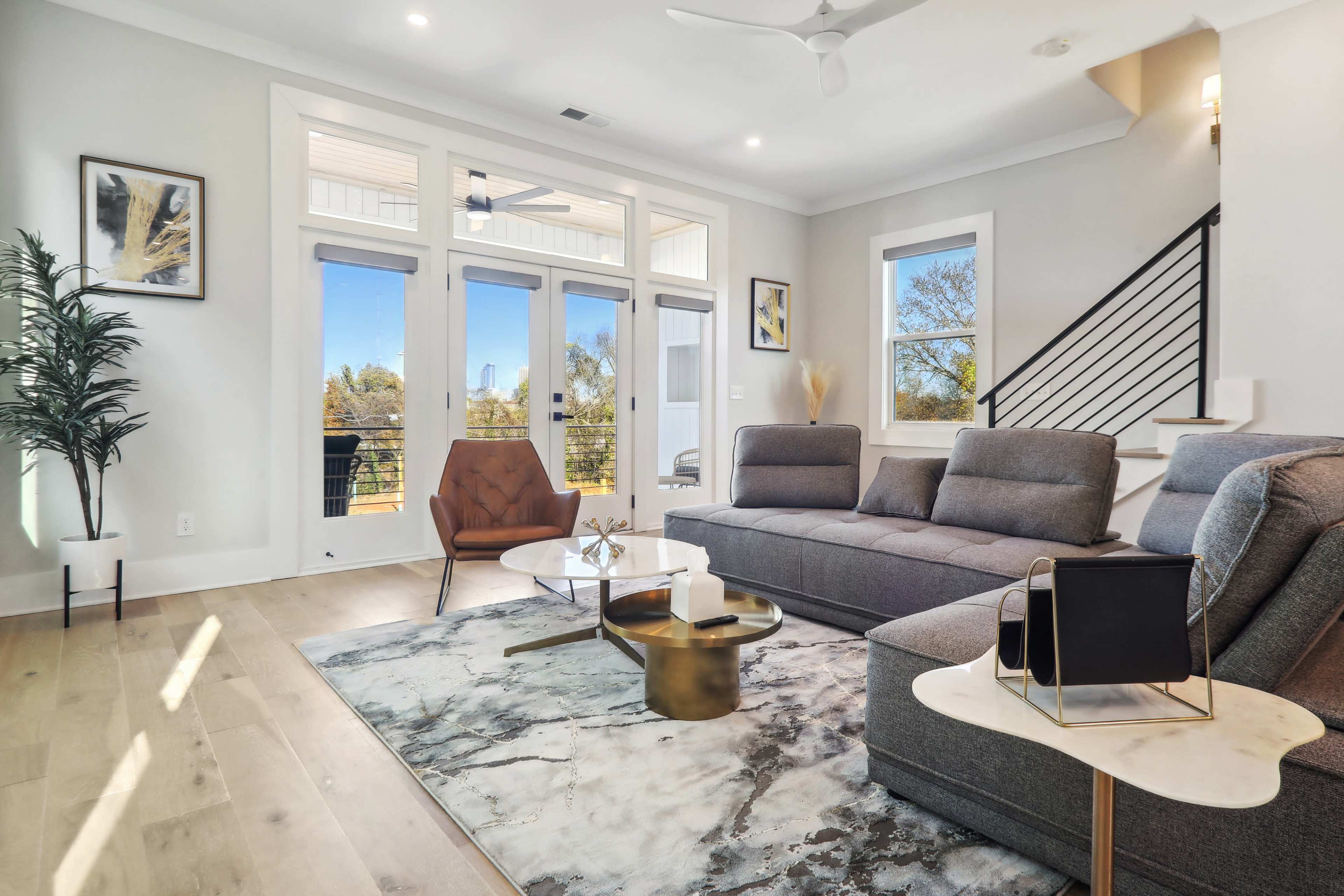 The living room features a modern sofa arrangement, a coffee table, and large windows that provide a view of the exterior.