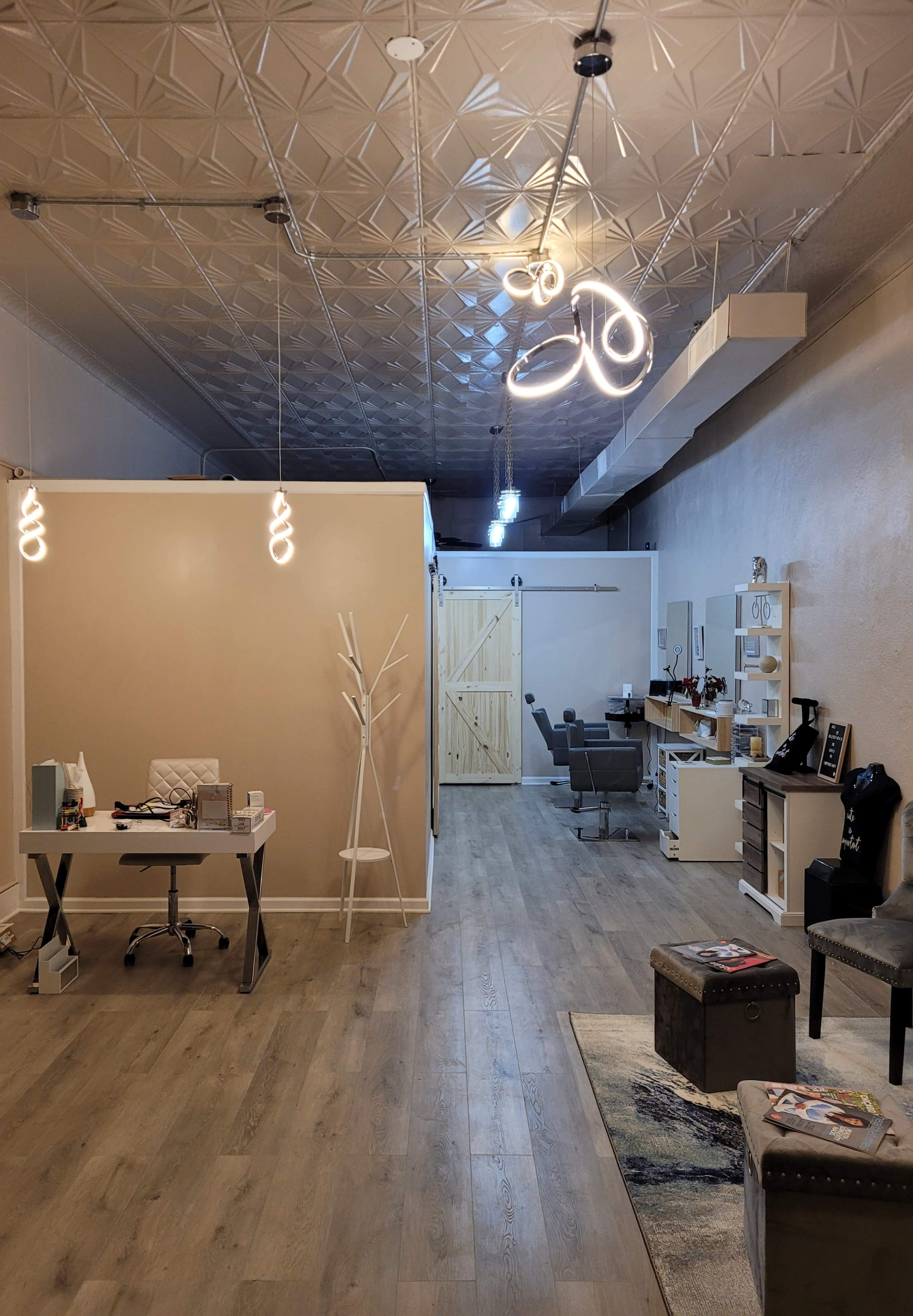 A modern interior of a salon or office space with a reception area, stylist chairs in the background, and unique light fixtures hanging from the ceiling.
