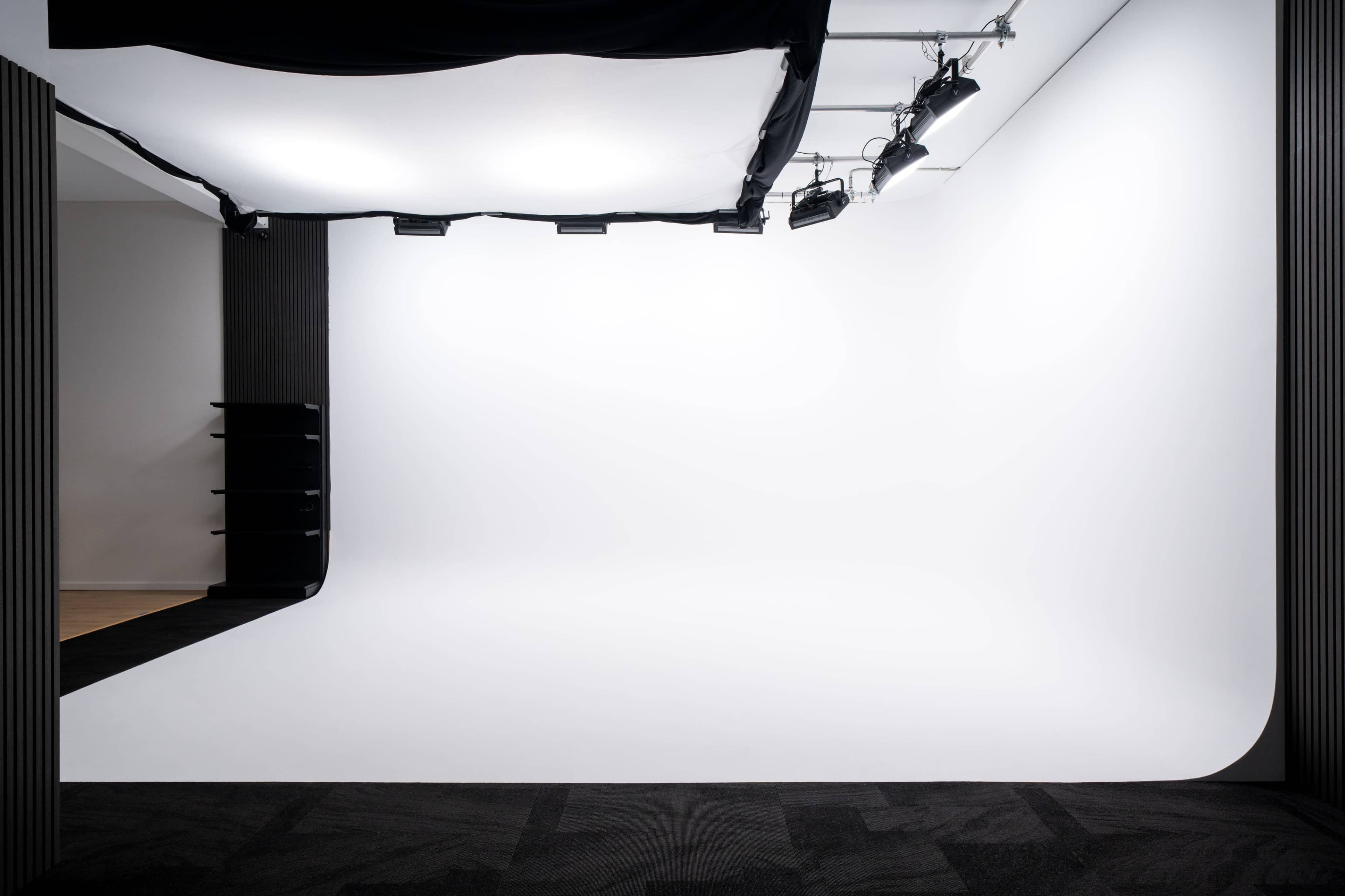 The image shows a spacious photography studio with a seamless white backdrop and overhead lighting.