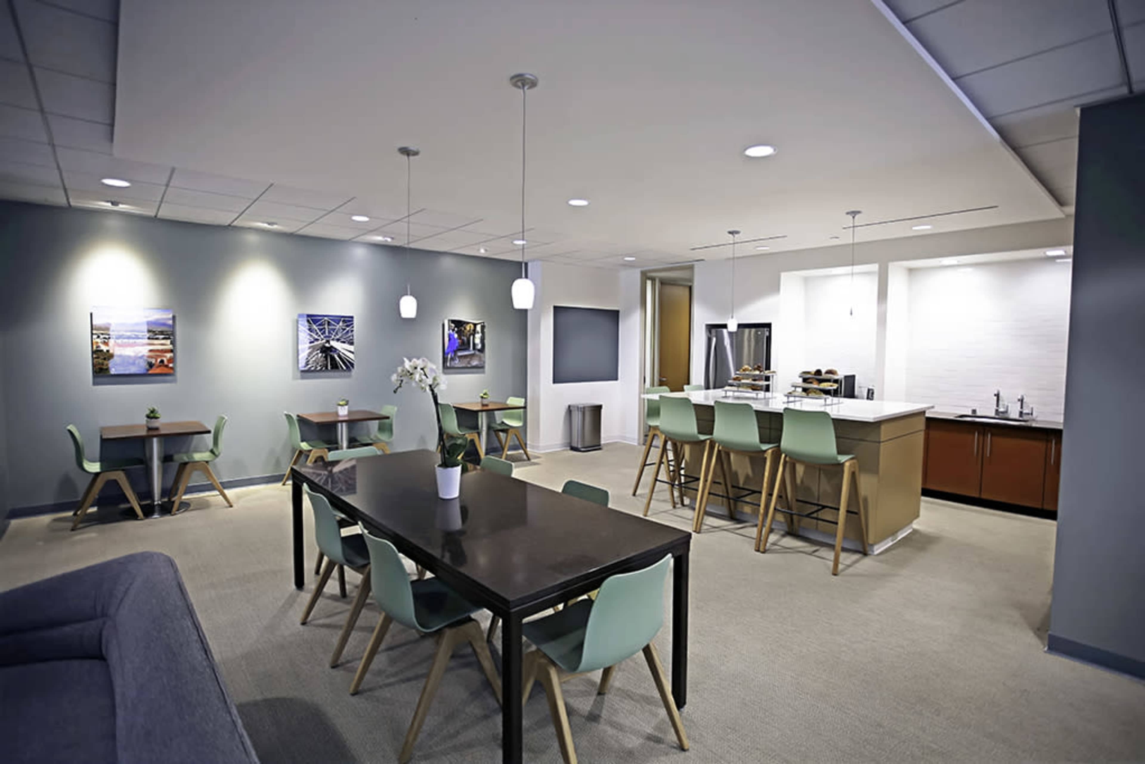 A modern communal space featuring a kitchen area with a bar, several tables, and wall art.