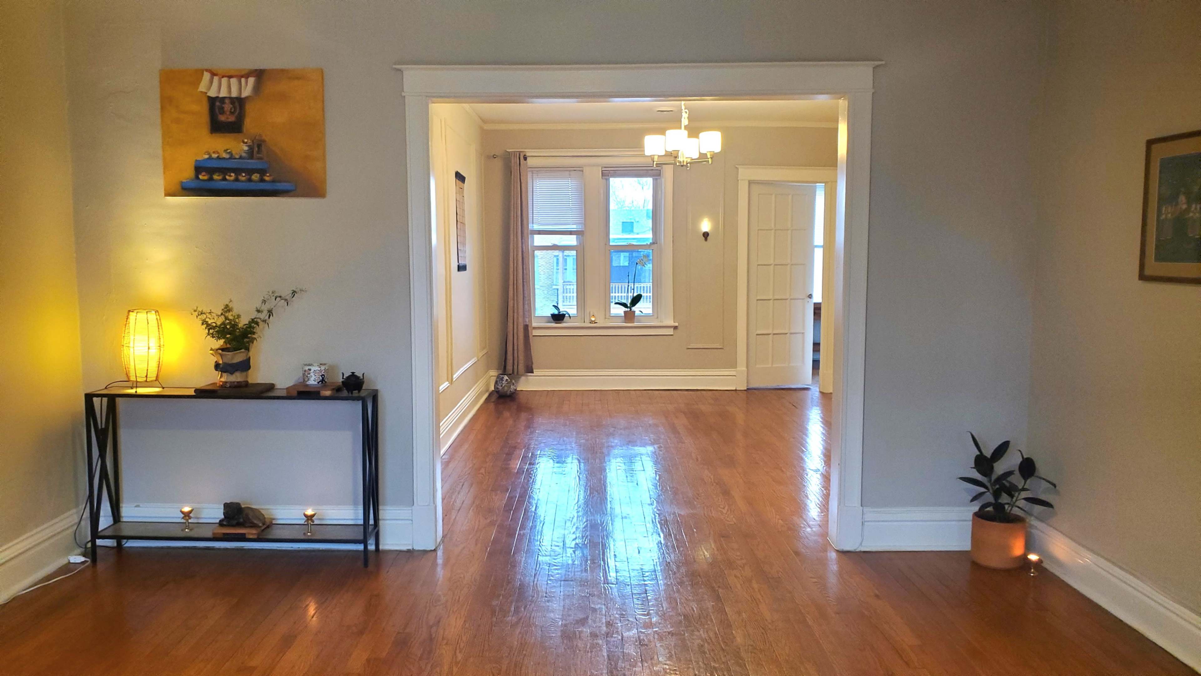 The image shows a spacious hallway leading to a well-lit room with wooden floors and decorative elements on the walls.