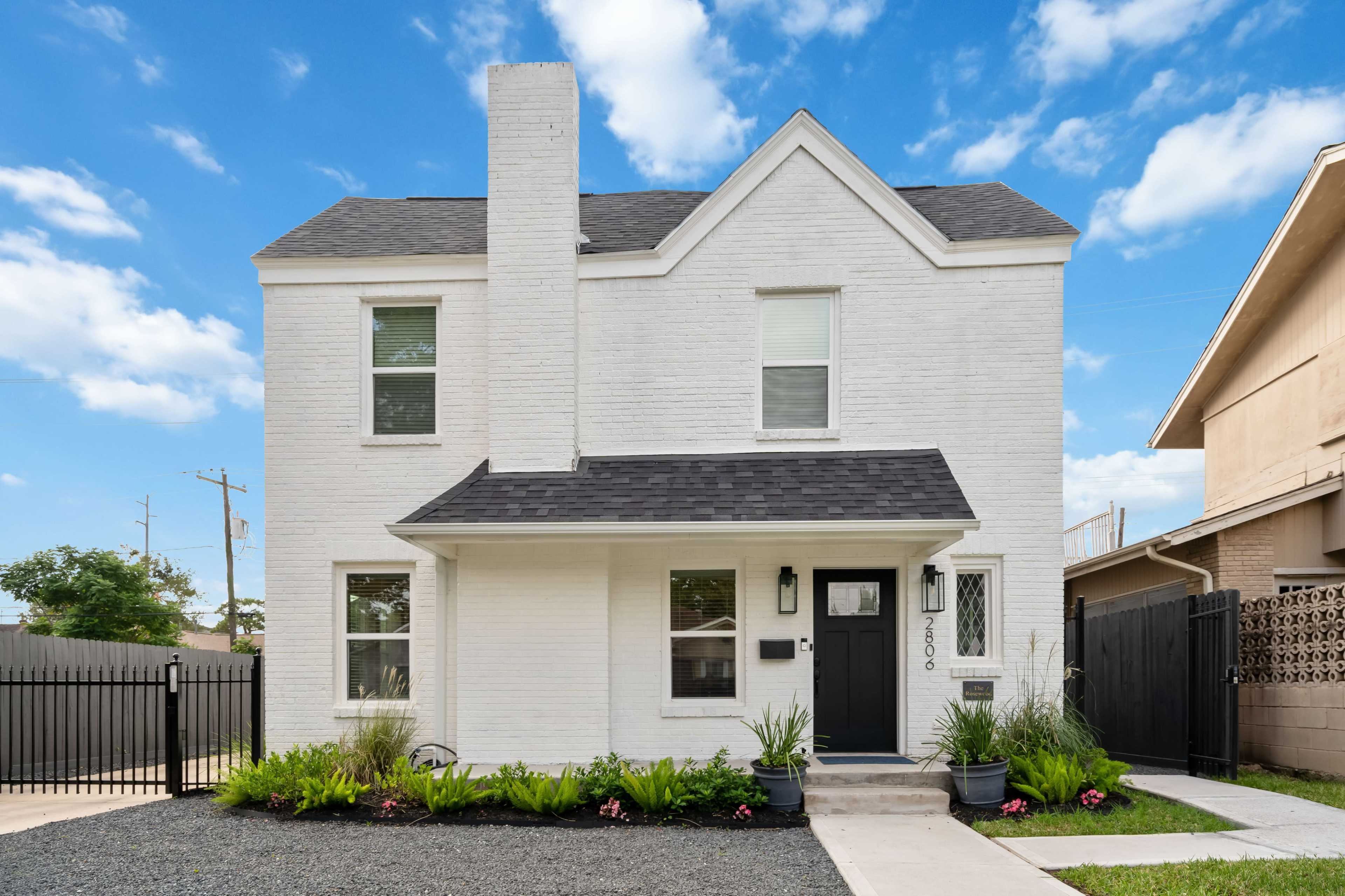 A two-story white brick house with a black roof and a neatly landscaped front yard.