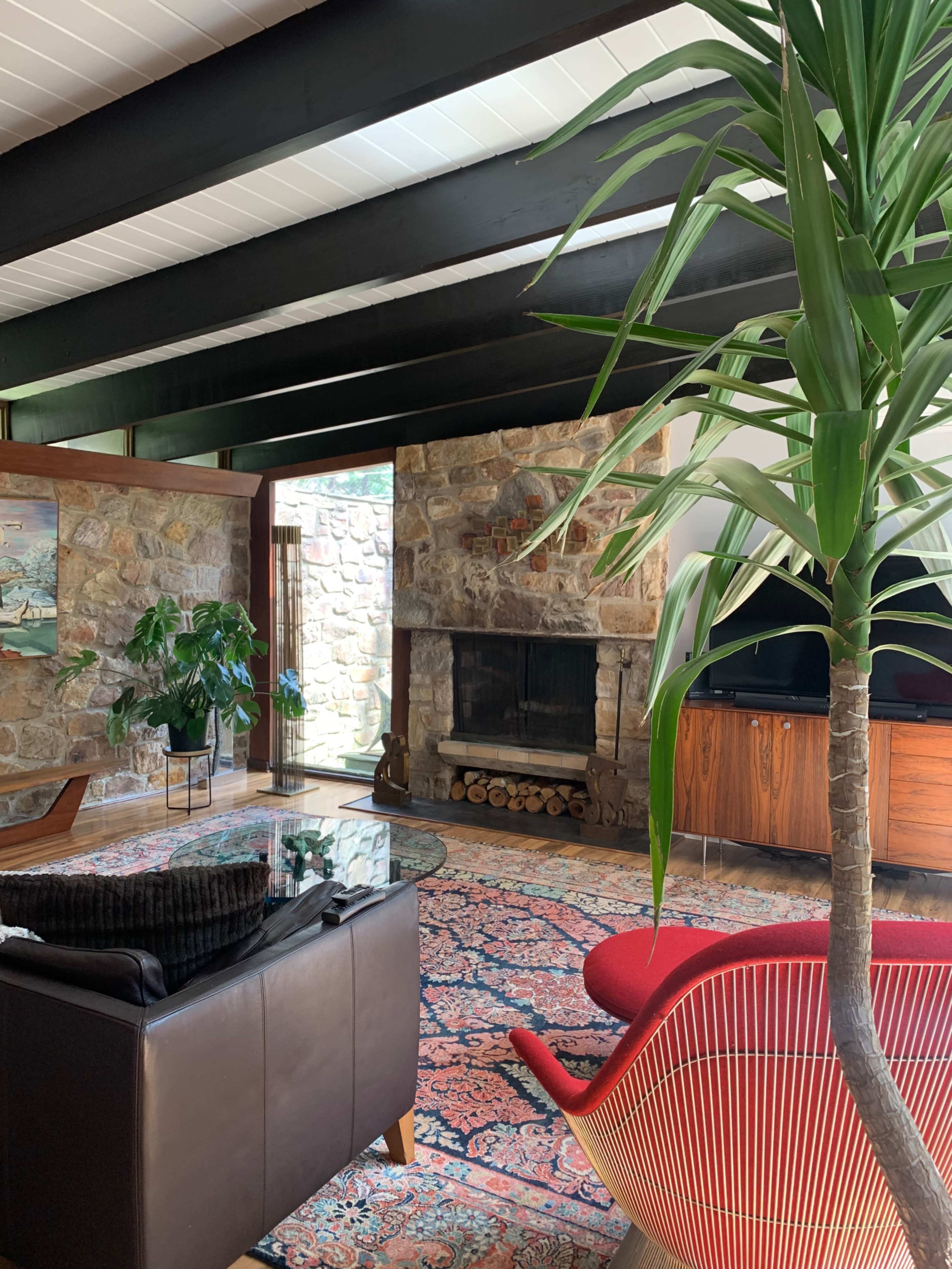 A spacious living room with stone walls, wooden beams, a cozy fireplace, a large glass coffee table, and a red accent chair.