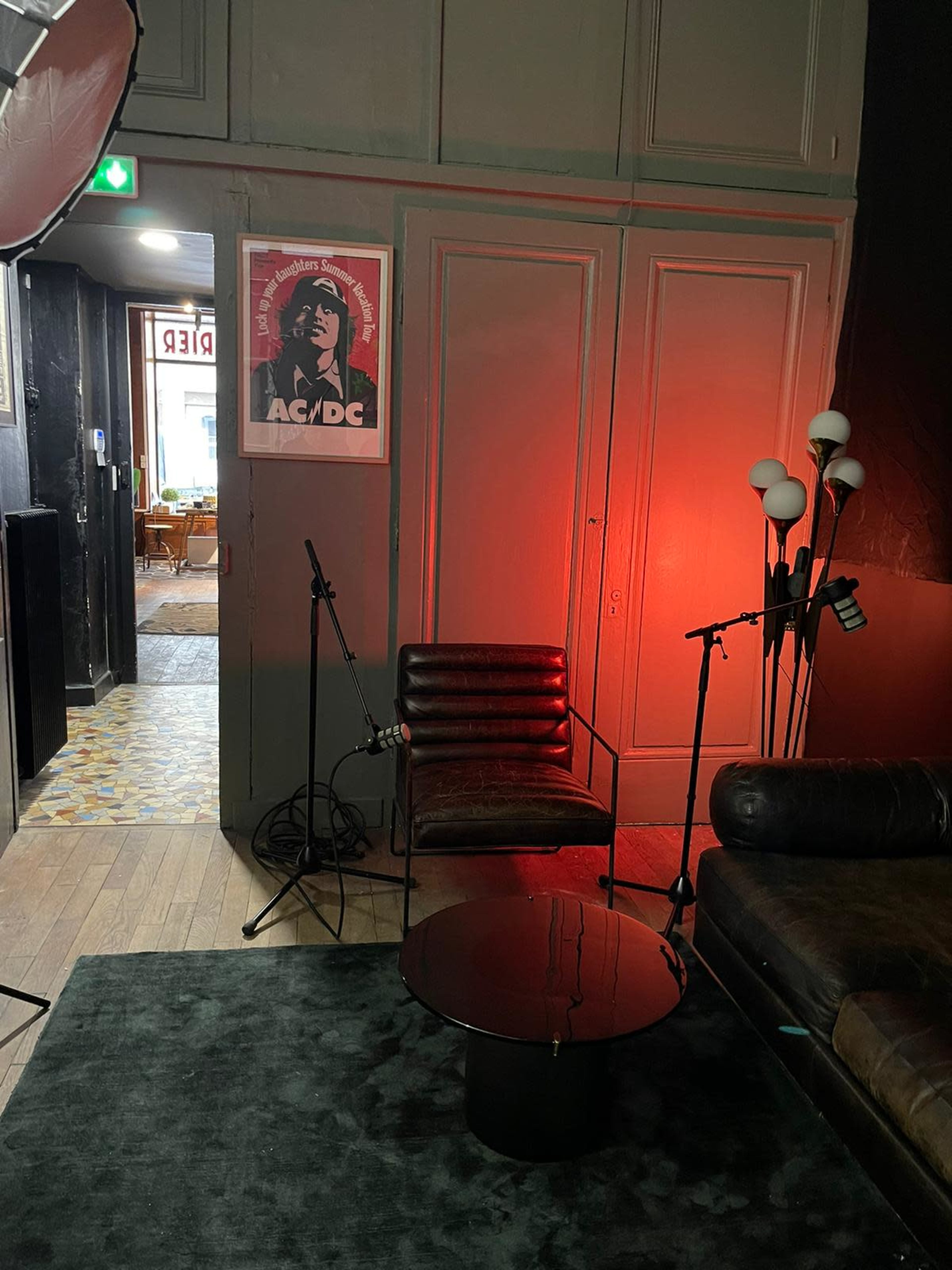 A cozy room with a chair, a small table, and microphones set up, featuring an AC/DC poster on the wall.