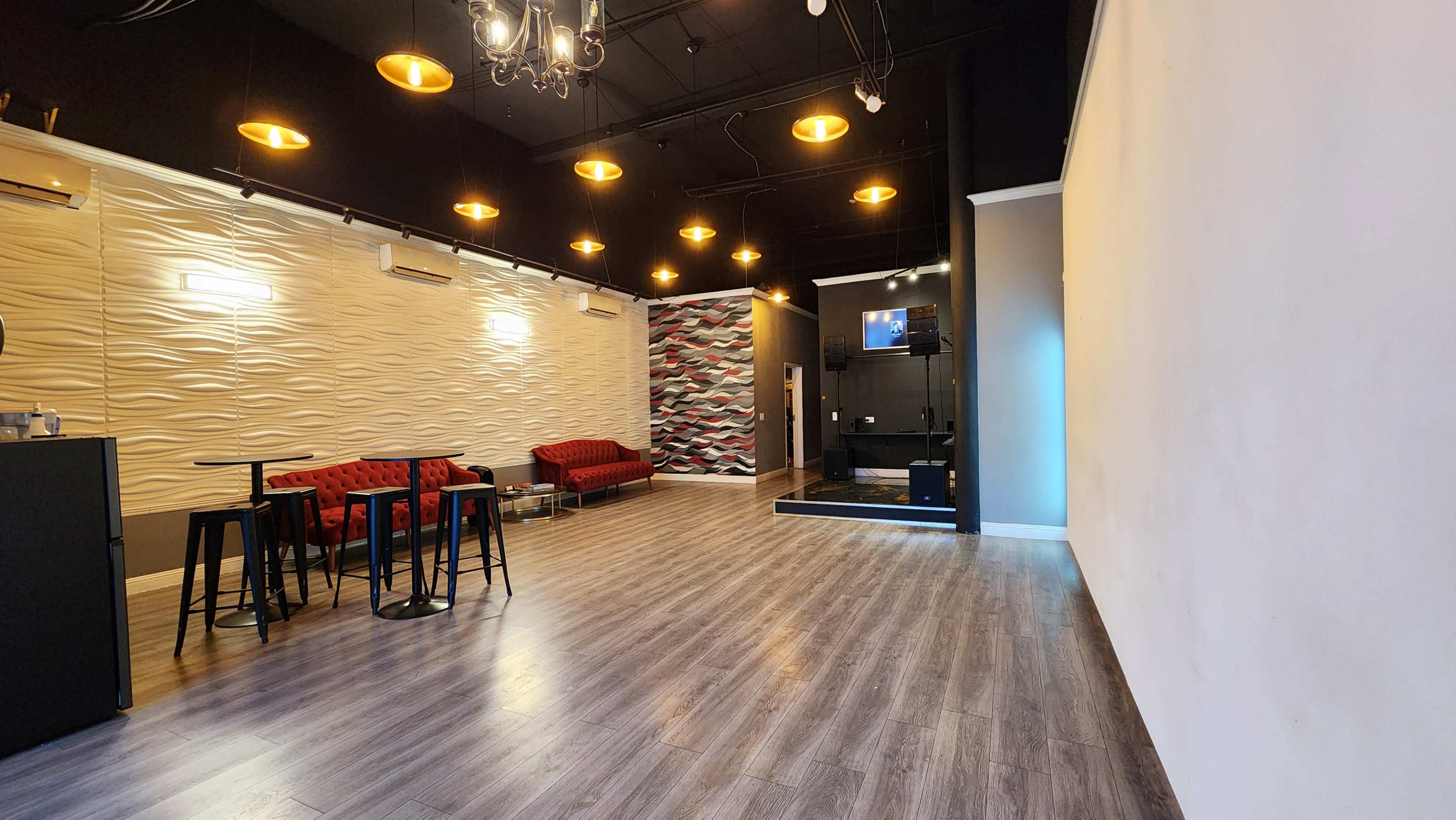 A spacious indoor area with wooden flooring, featuring a lounge section with red sofas, small black tables, and a wall decorated with wavy textures alongside a colored accent wall.