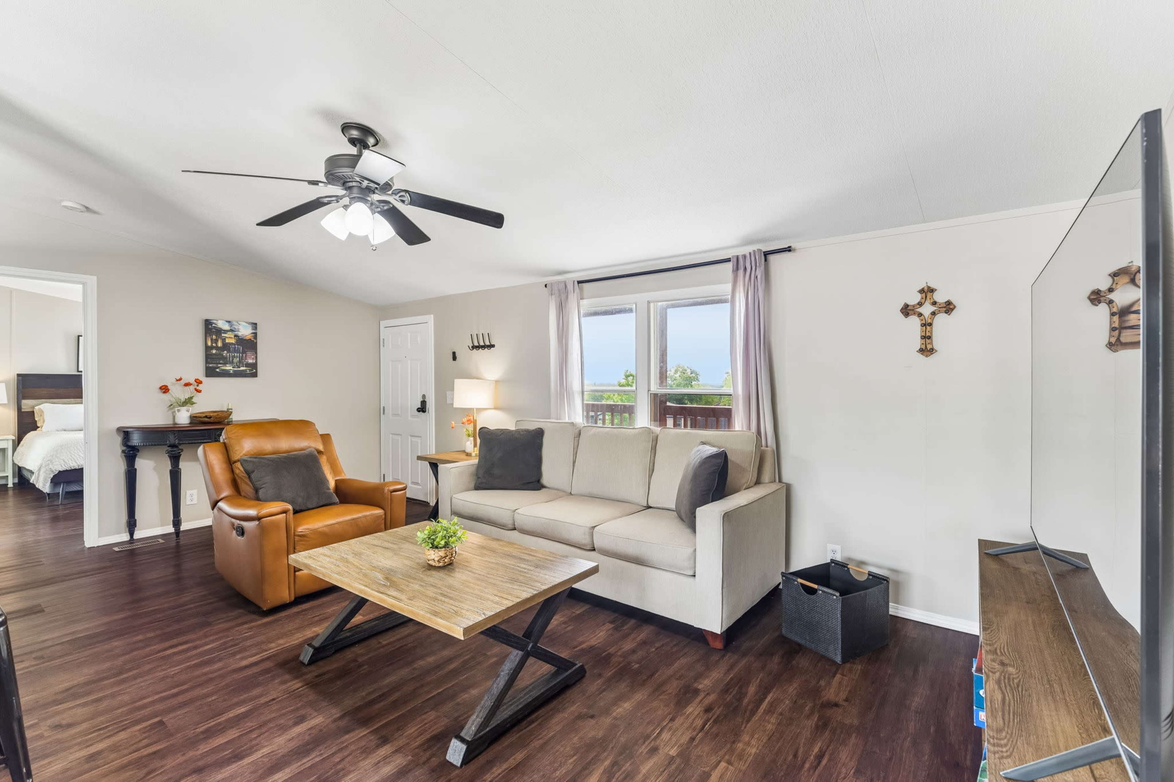 The living room features a couch, an armchair, a coffee table, and a television, with a window offering natural light.