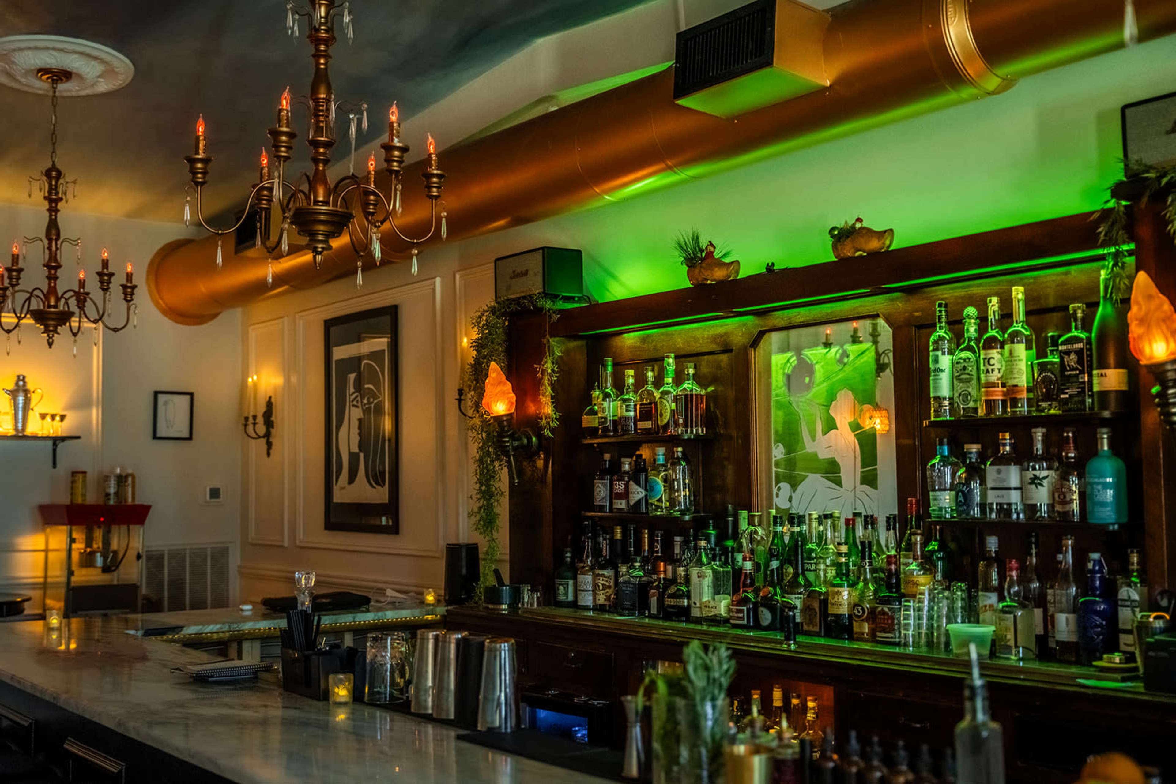 A well-stocked bar with a variety of bottles on the shelves, illuminated by green lights and adorned with decorative elements.