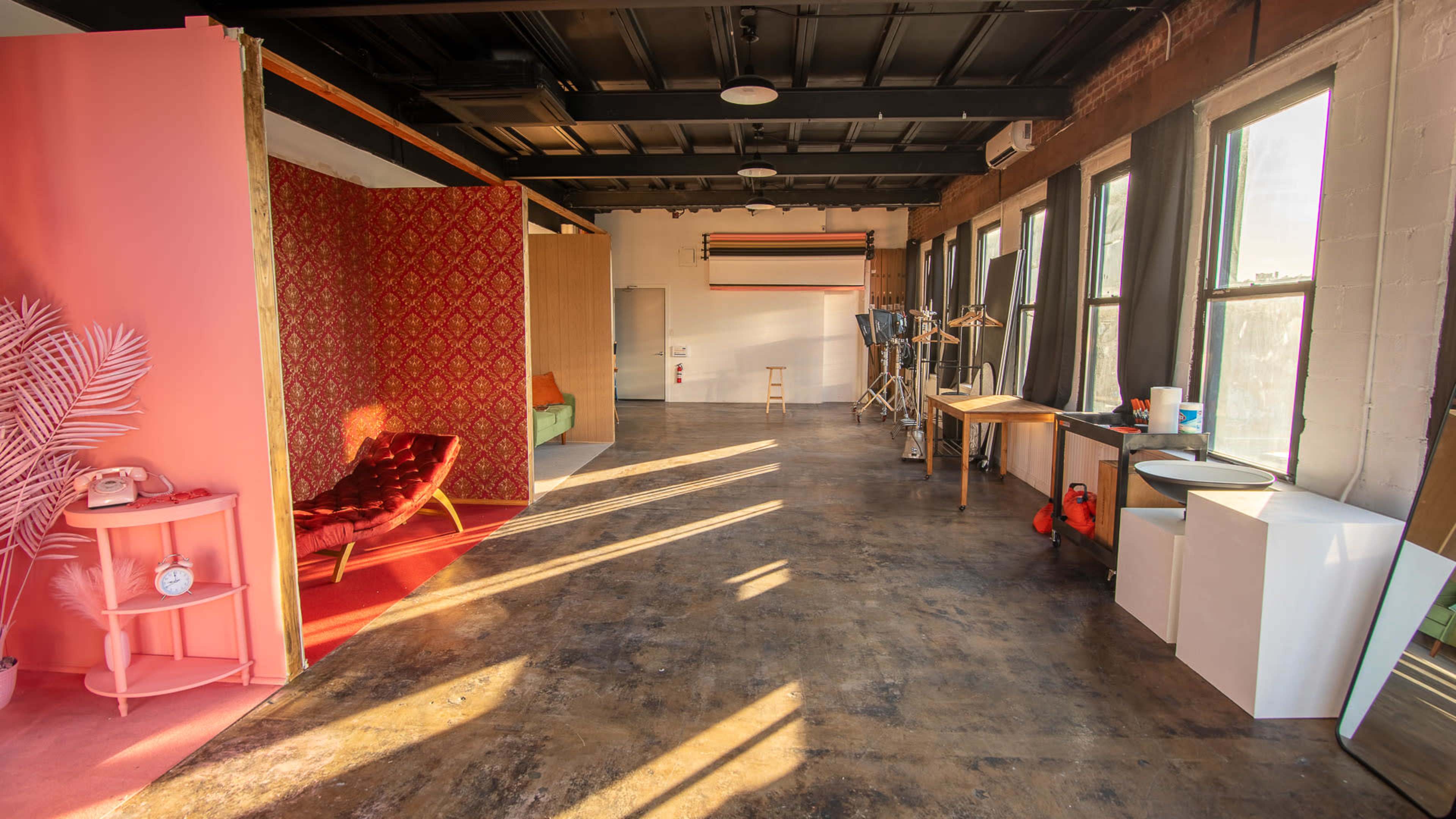 A spacious interior room with a polished concrete floor, distinct areas separated by colorful backdrops, and large windows allowing sunlight to stream in.
