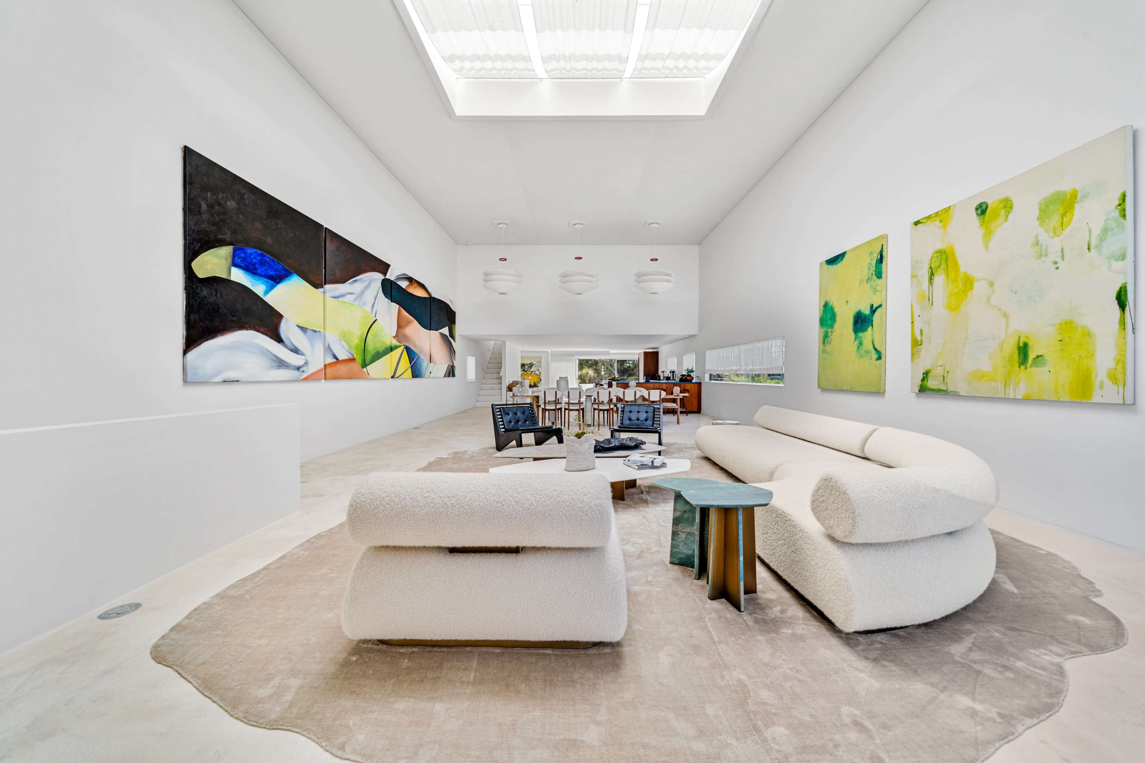 The image shows a spacious, modern interior featuring large abstract paintings on the walls, a plush beige sofa, and a central coffee table on a light rug.