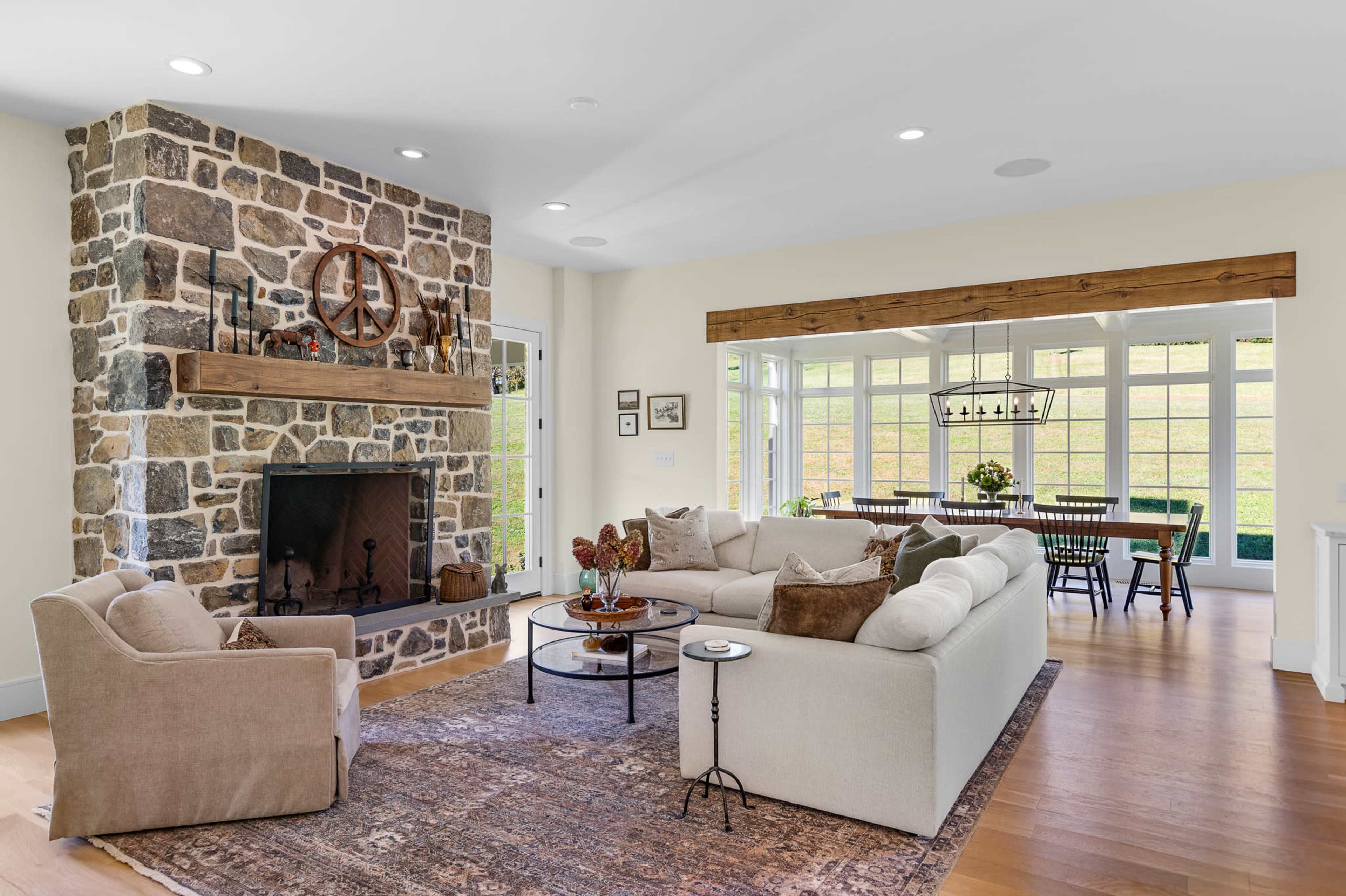 The image shows a modern living room with a stone fireplace, comfortable seating arrangements, and a dining area visible in the background.