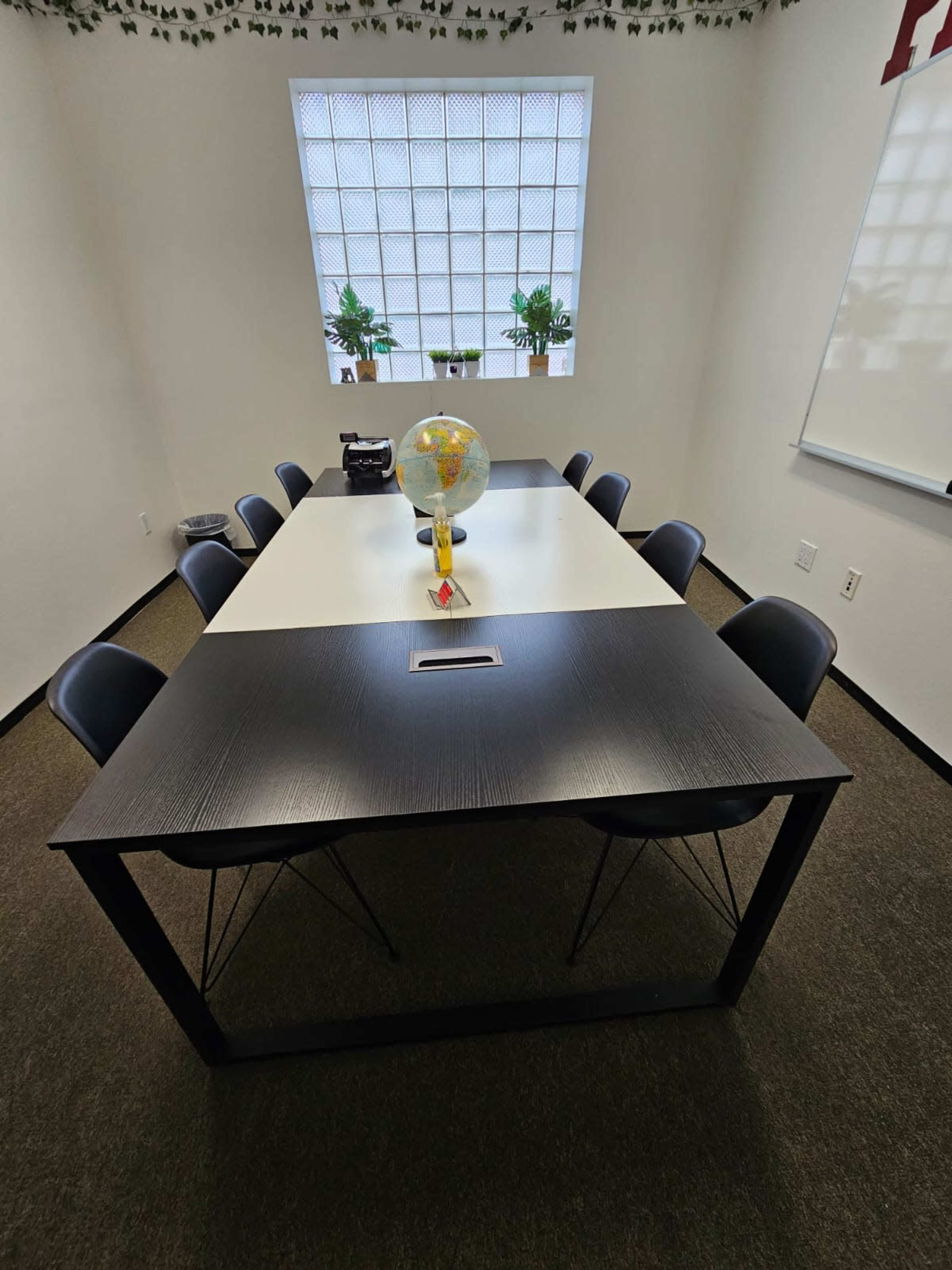 A rectangular conference room table is surrounded by eight chairs, with a globe and a plant centerpiece on the table.