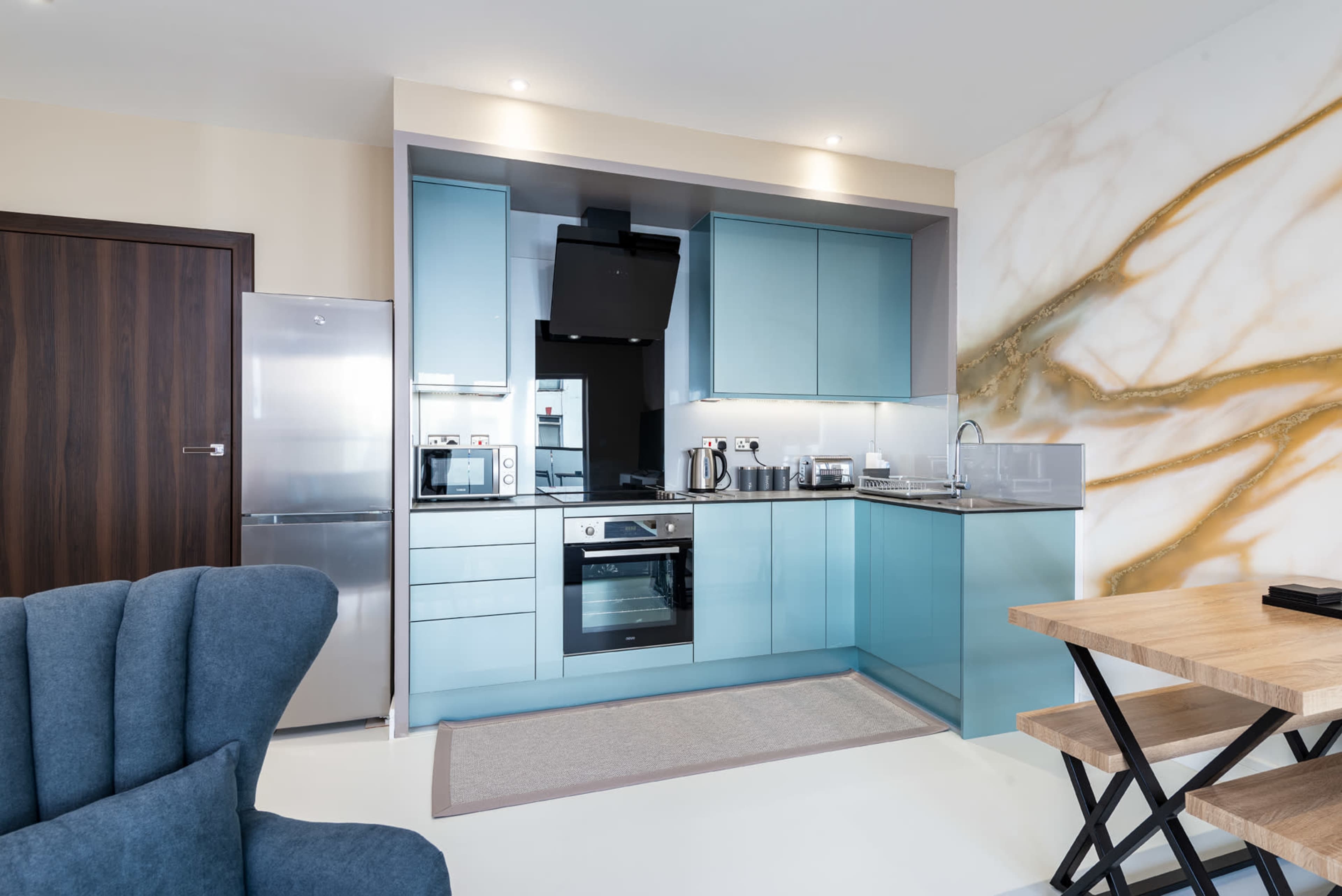 A modern kitchen with blue cabinetry, stainless steel appliances, and a wooden dining table.
