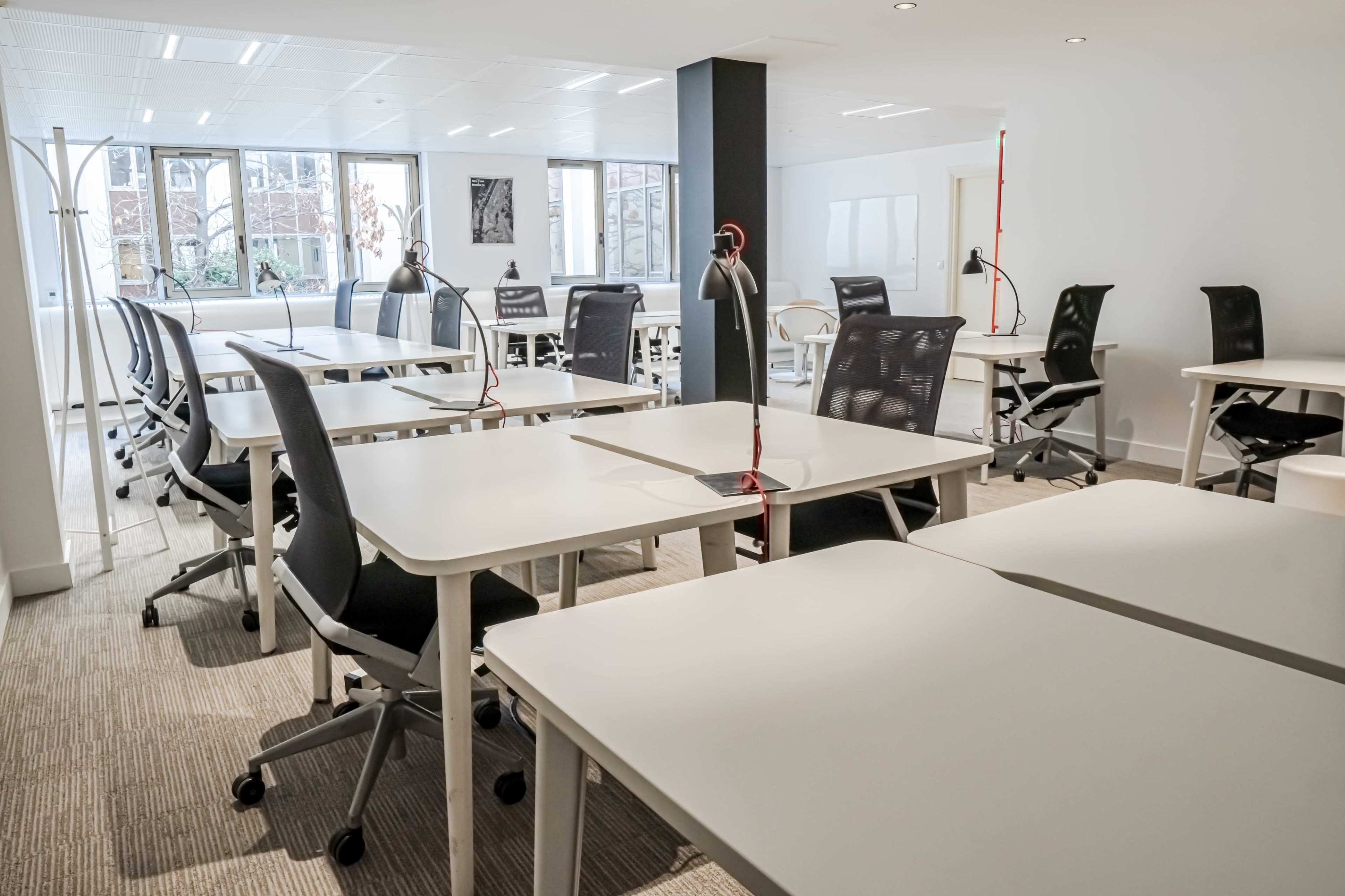 A spacious office area with multiple desks and chairs arranged neatly under bright windows.