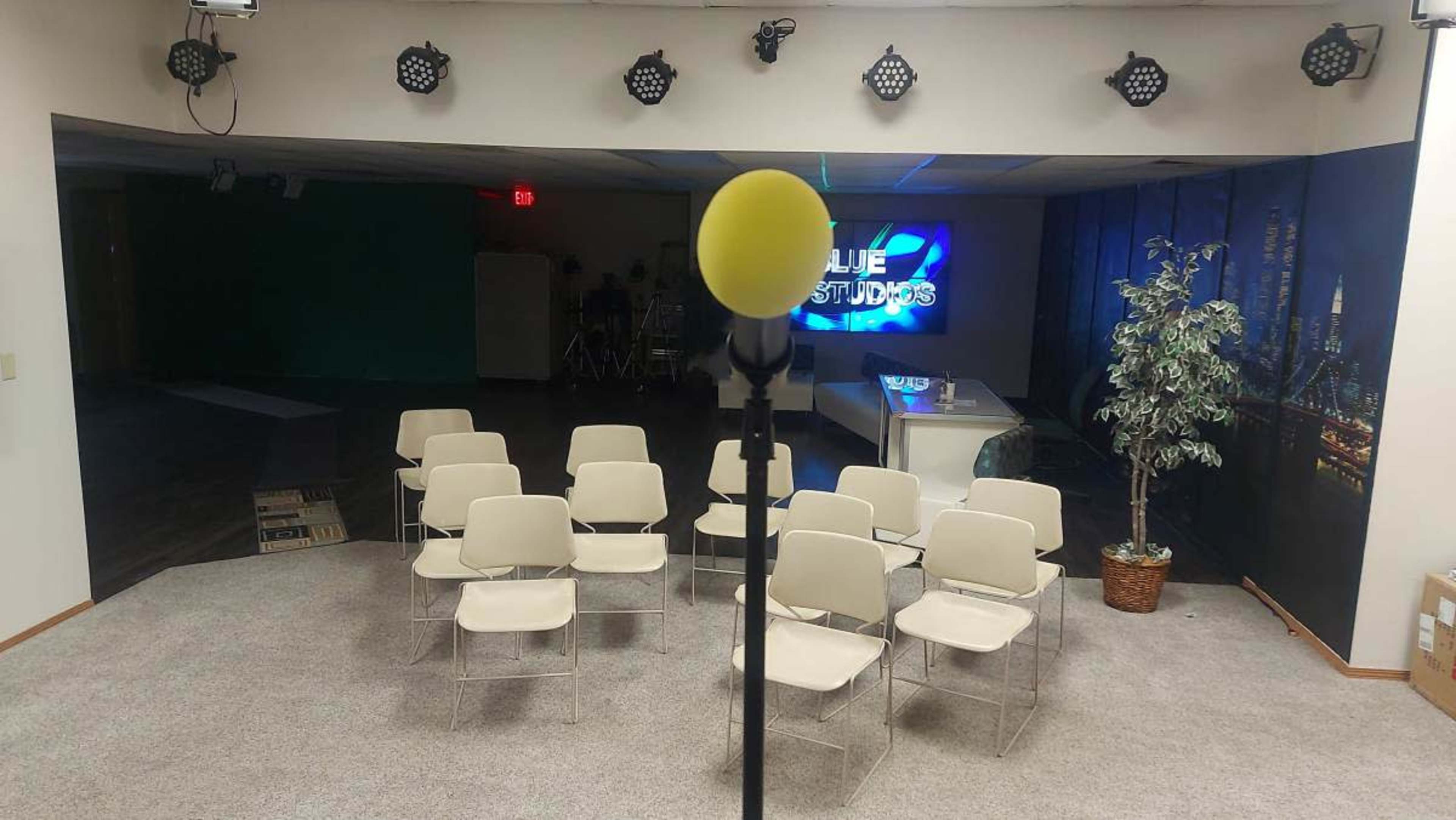 A microphone on a stand is positioned in front of a seated audience setup in a studio with a green screen and a "Blue Studios" sign in the background.