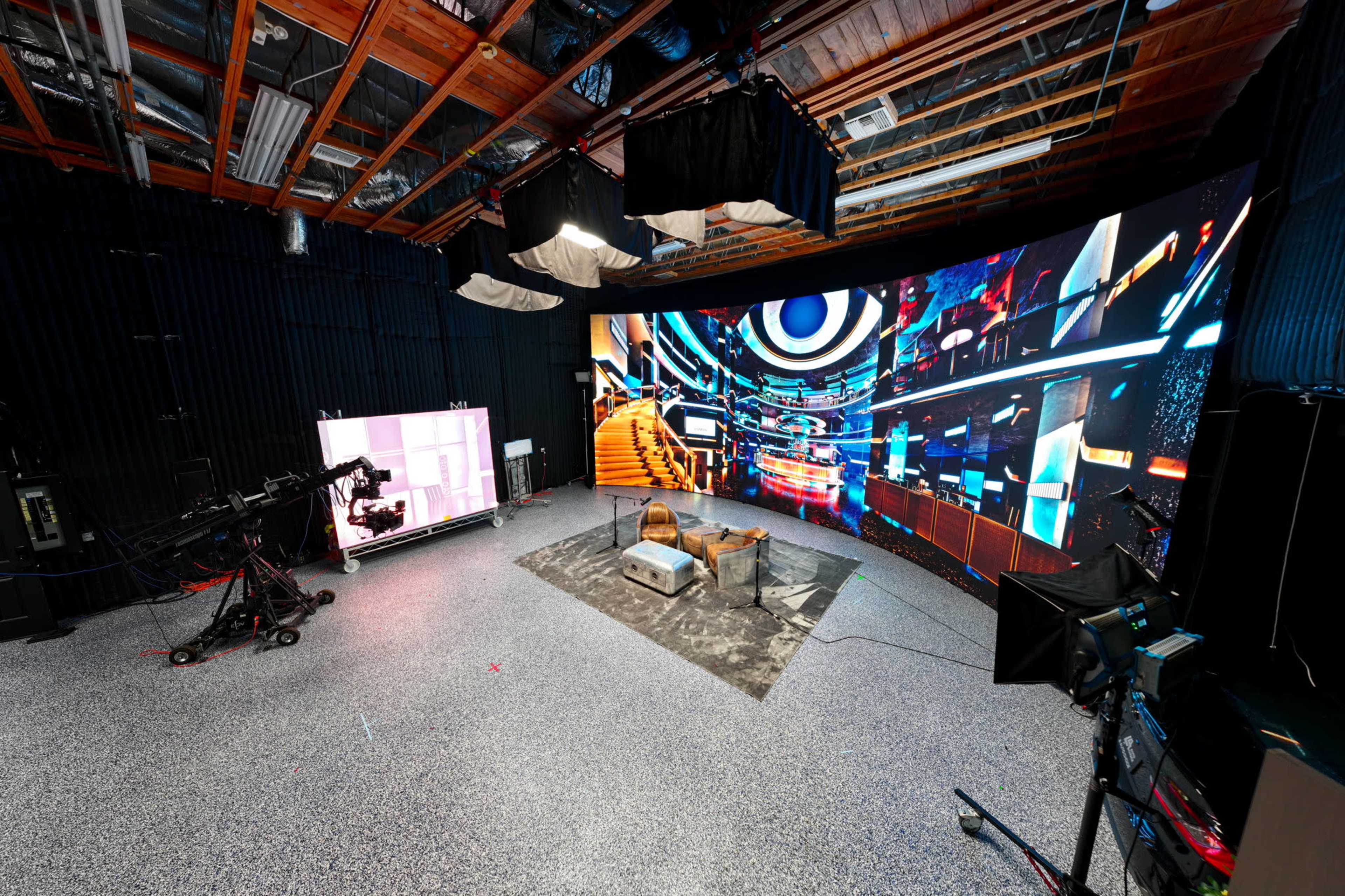 The image shows a modern film studio equipped with a large circular display and camera setup, surrounded by various lights and equipment.