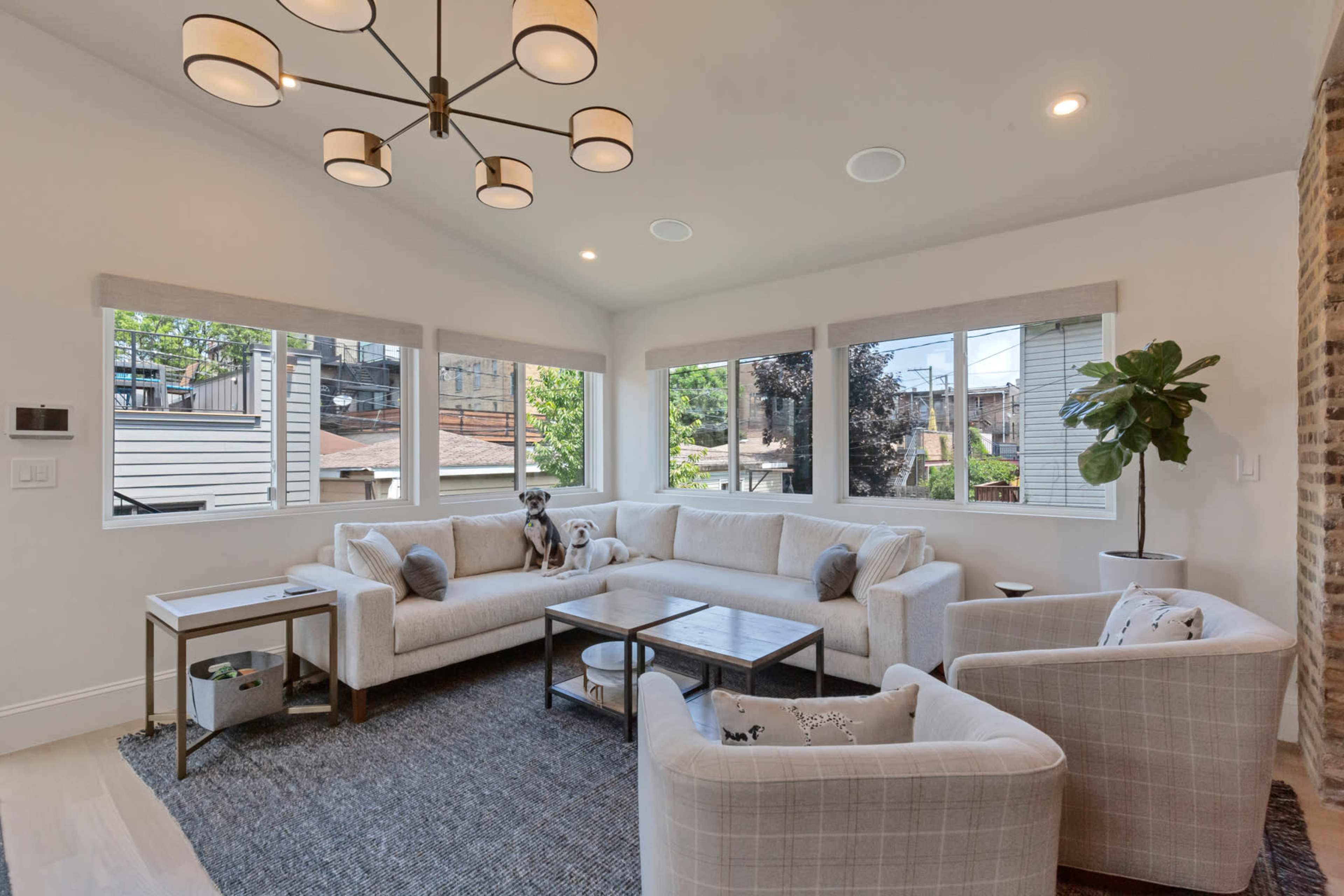 The image shows a modern living room with a sectional sofa, armchairs, a coffee table, and large windows allowing natural light to enter.