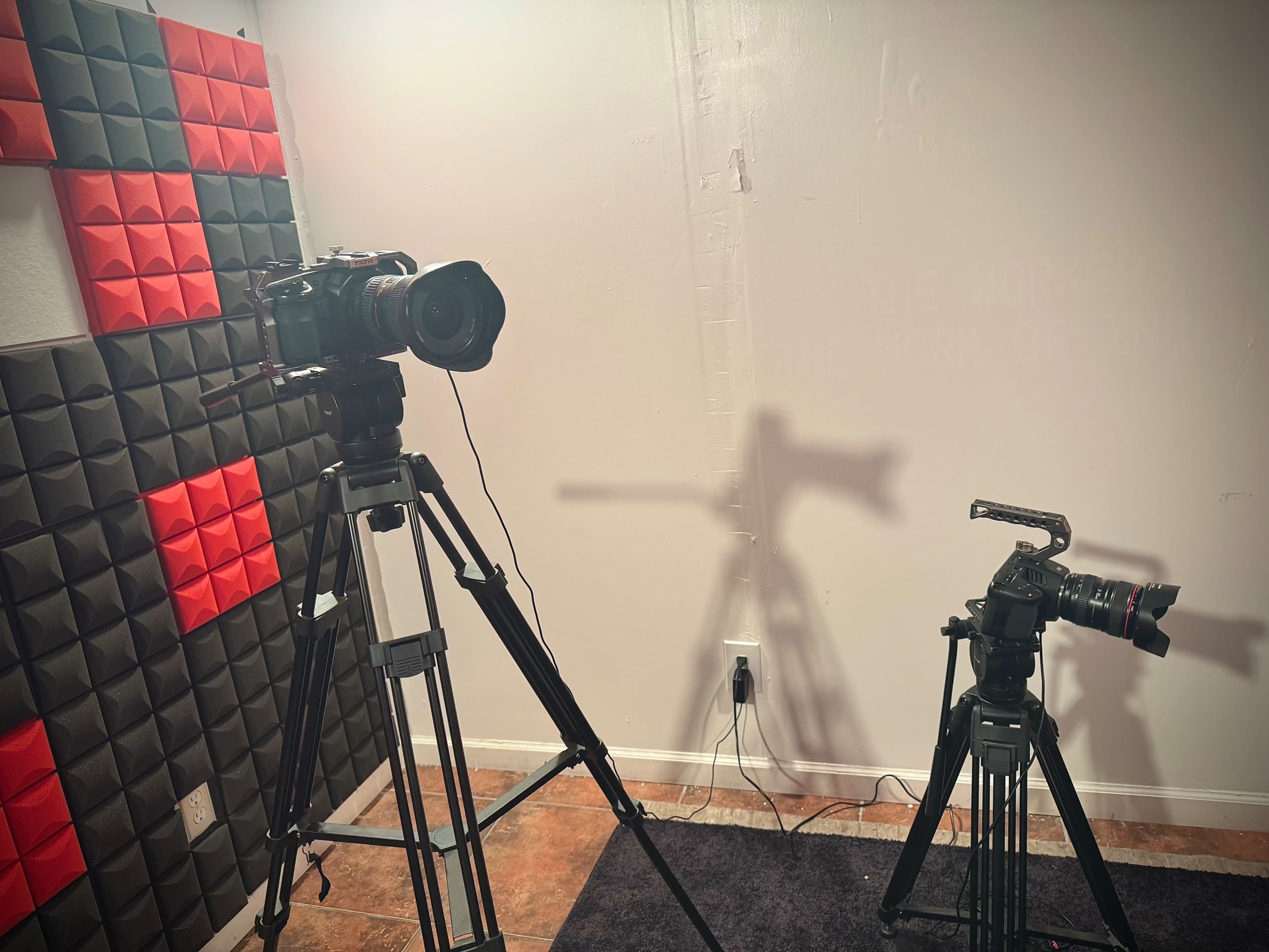 The image shows two cameras mounted on tripods in a room with red and black soundproofing panels on the walls.