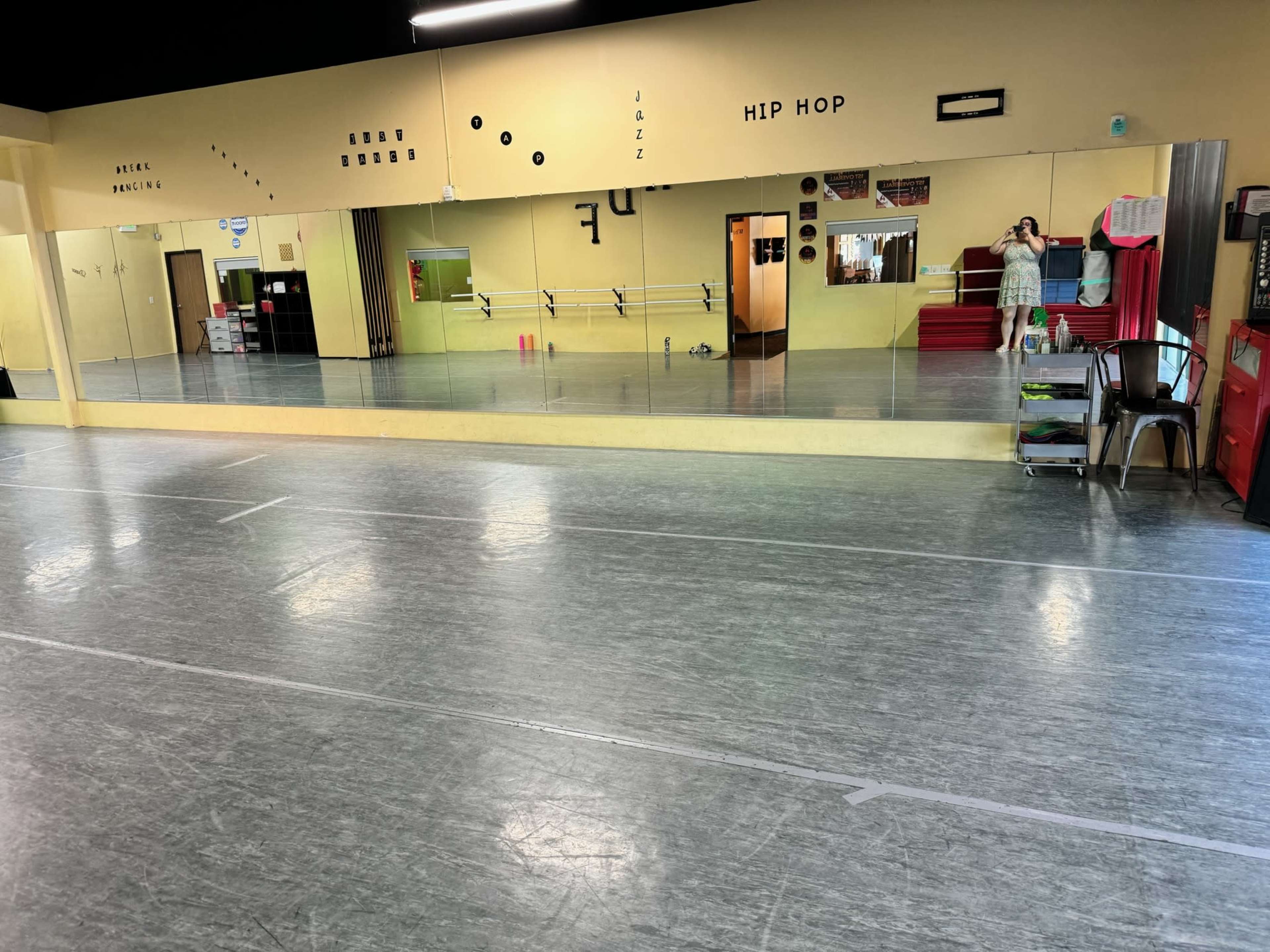 A spacious dance studio featuring mirrored walls, a smooth floor, and various sound and class labels on the walls.
