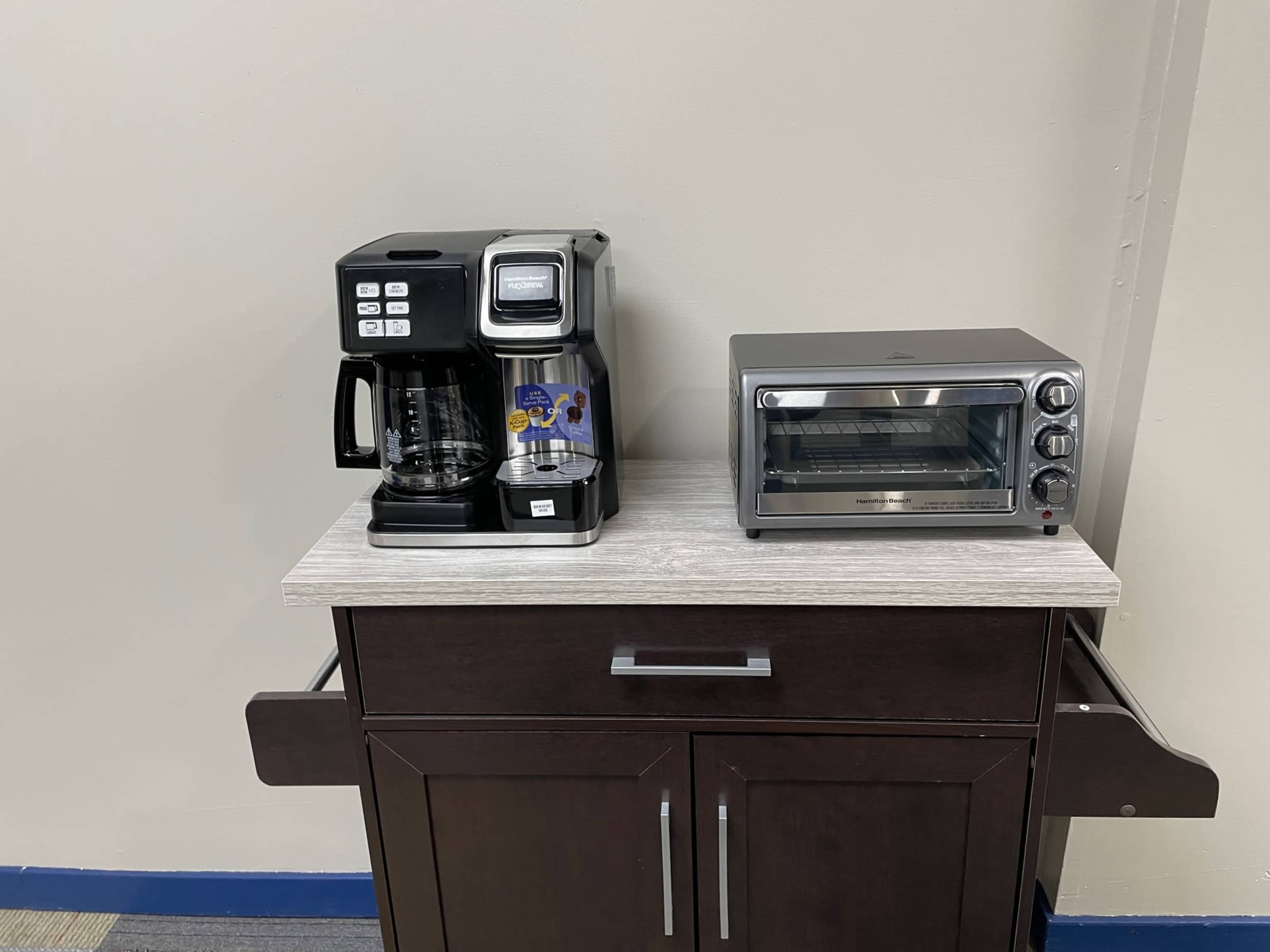 A coffee maker and a toaster oven placed side by side on a wooden kitchen cart.