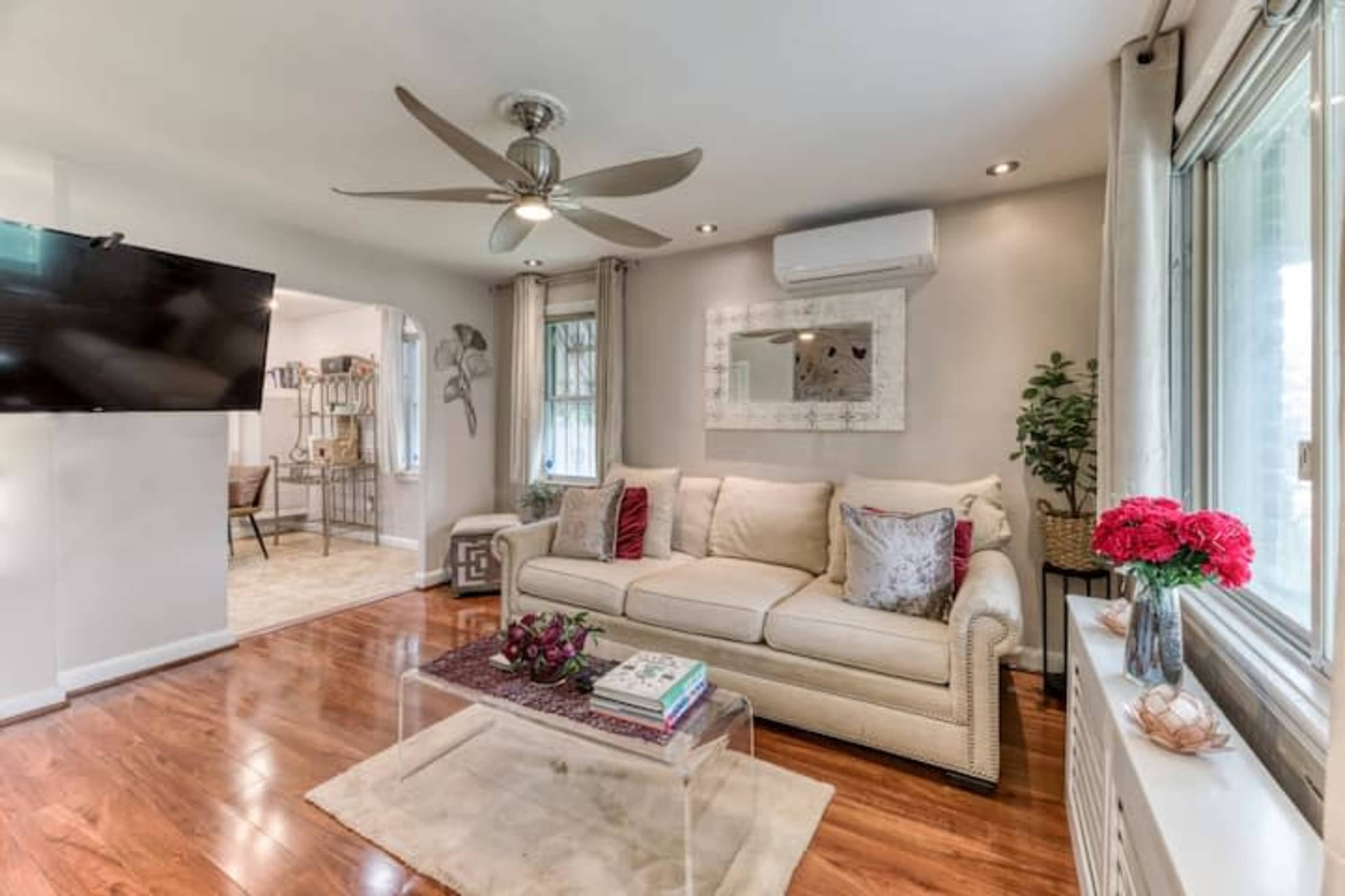 A living room with a light-colored sofa, a flat-screen television mounted on the wall, and a coffee table on a rug.