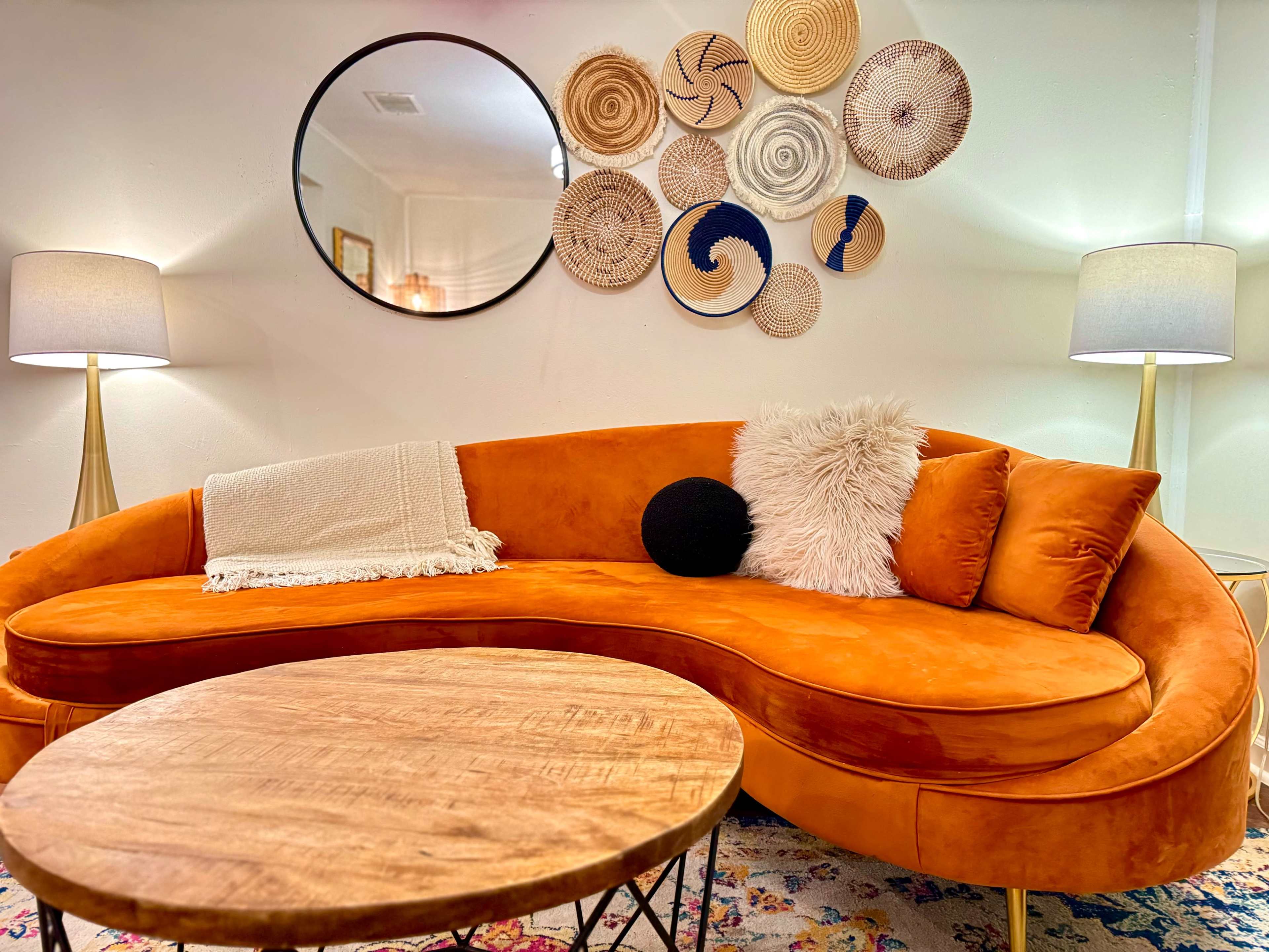 A curved orange sofa sits in a living room adorned with a wooden coffee table and decorative woven wall hangings above.