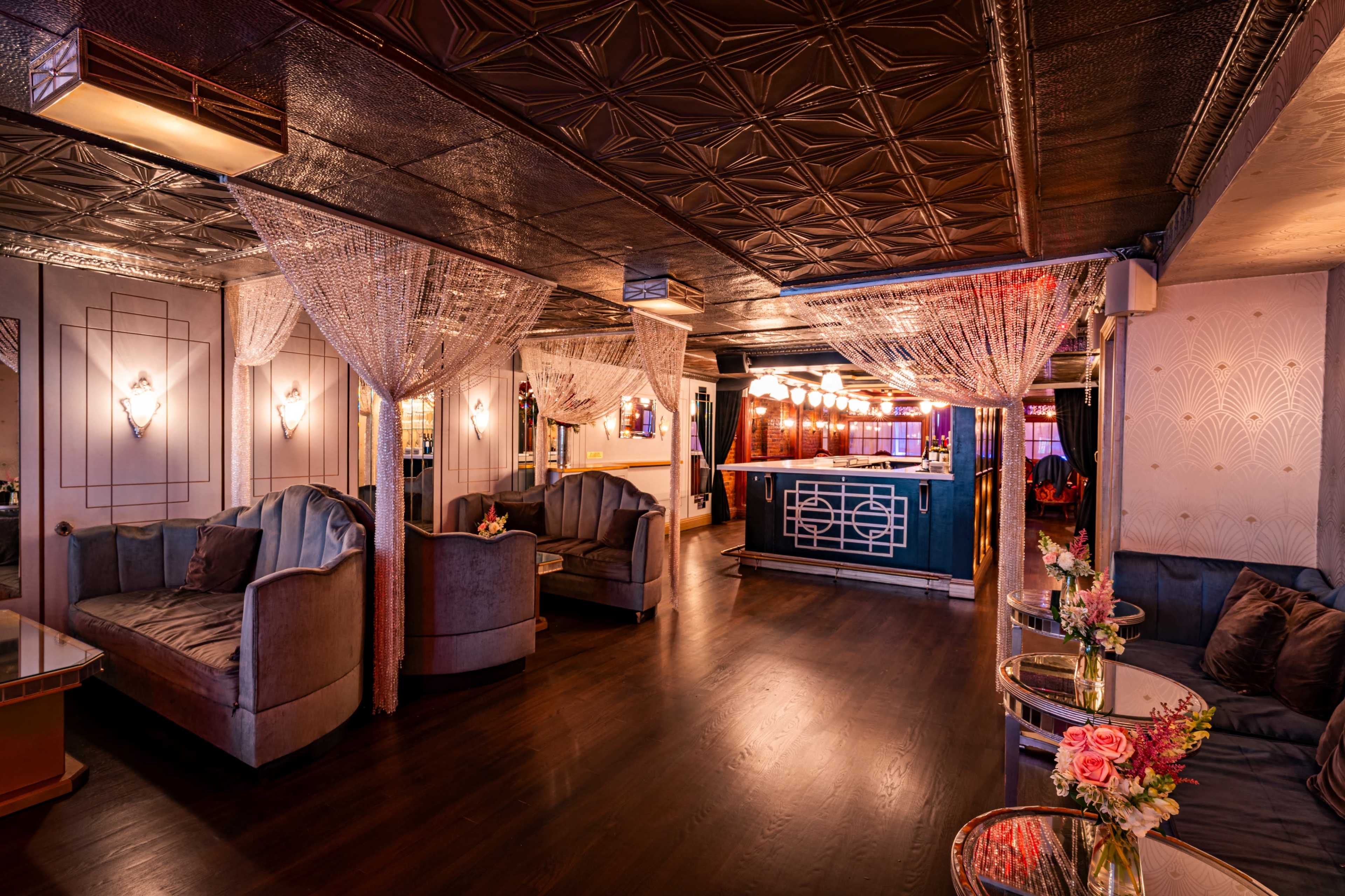 The image shows a stylish interior of a lounge featuring plush seating, ambient lighting, and an elegant bar area.