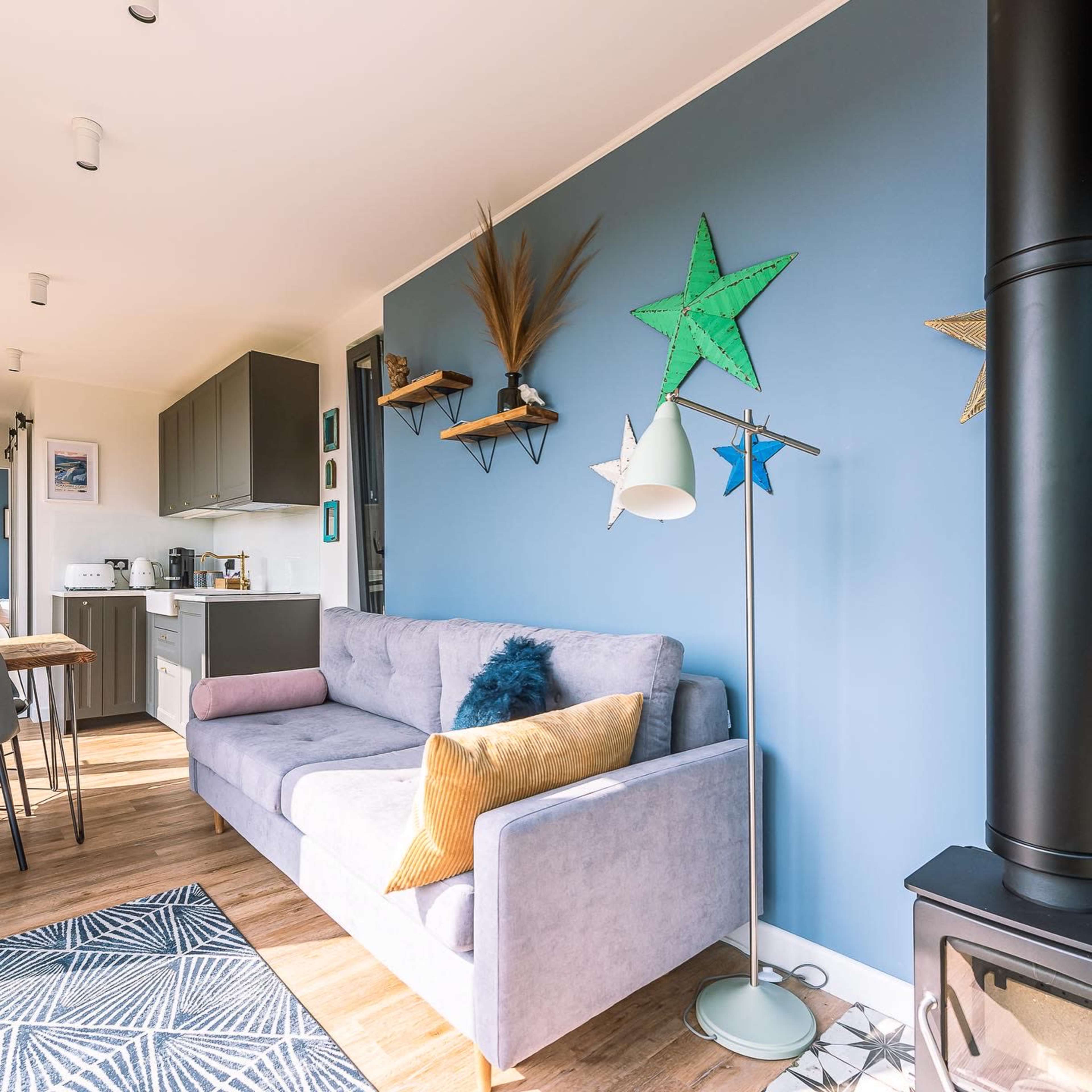 A modern living room with a gray couch, decorative stars on a blue wall, and an open kitchen area in the background.