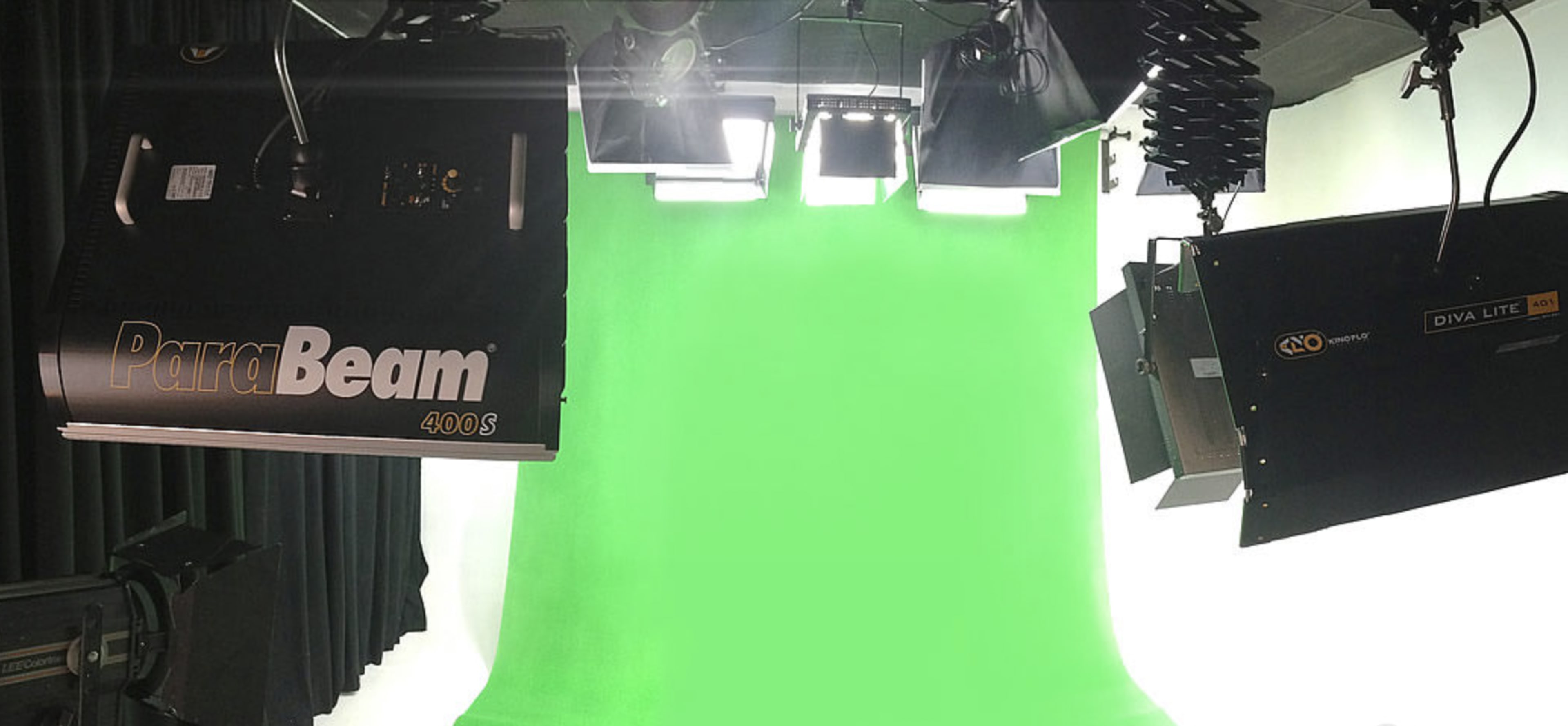 A photography studio with green screen backdrops and professional lighting equipment suspended from the ceiling.