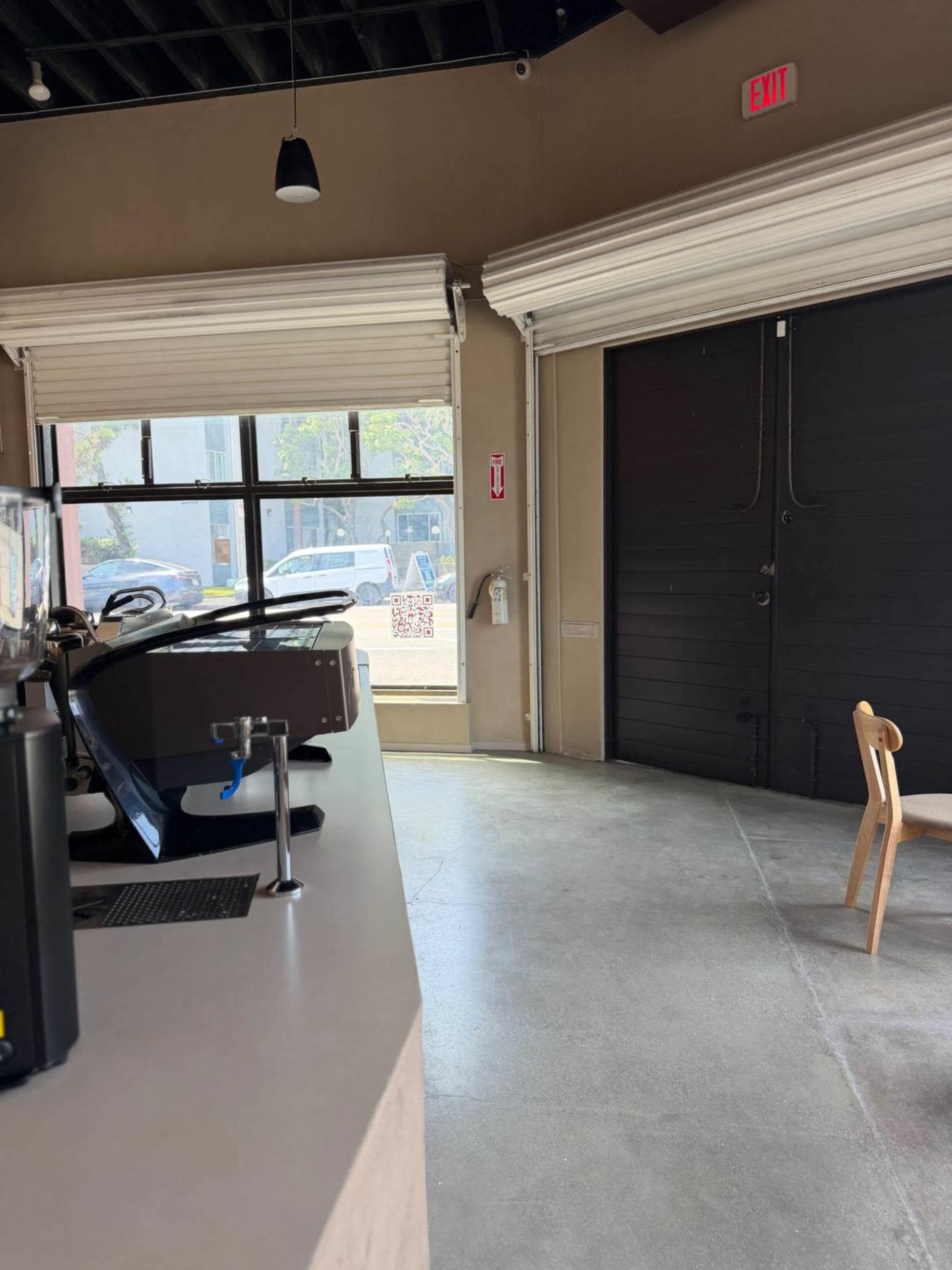 The image shows a modern coffee shop interior with a counter on the left, a window in the background, and a wooden chair positioned on the floor.