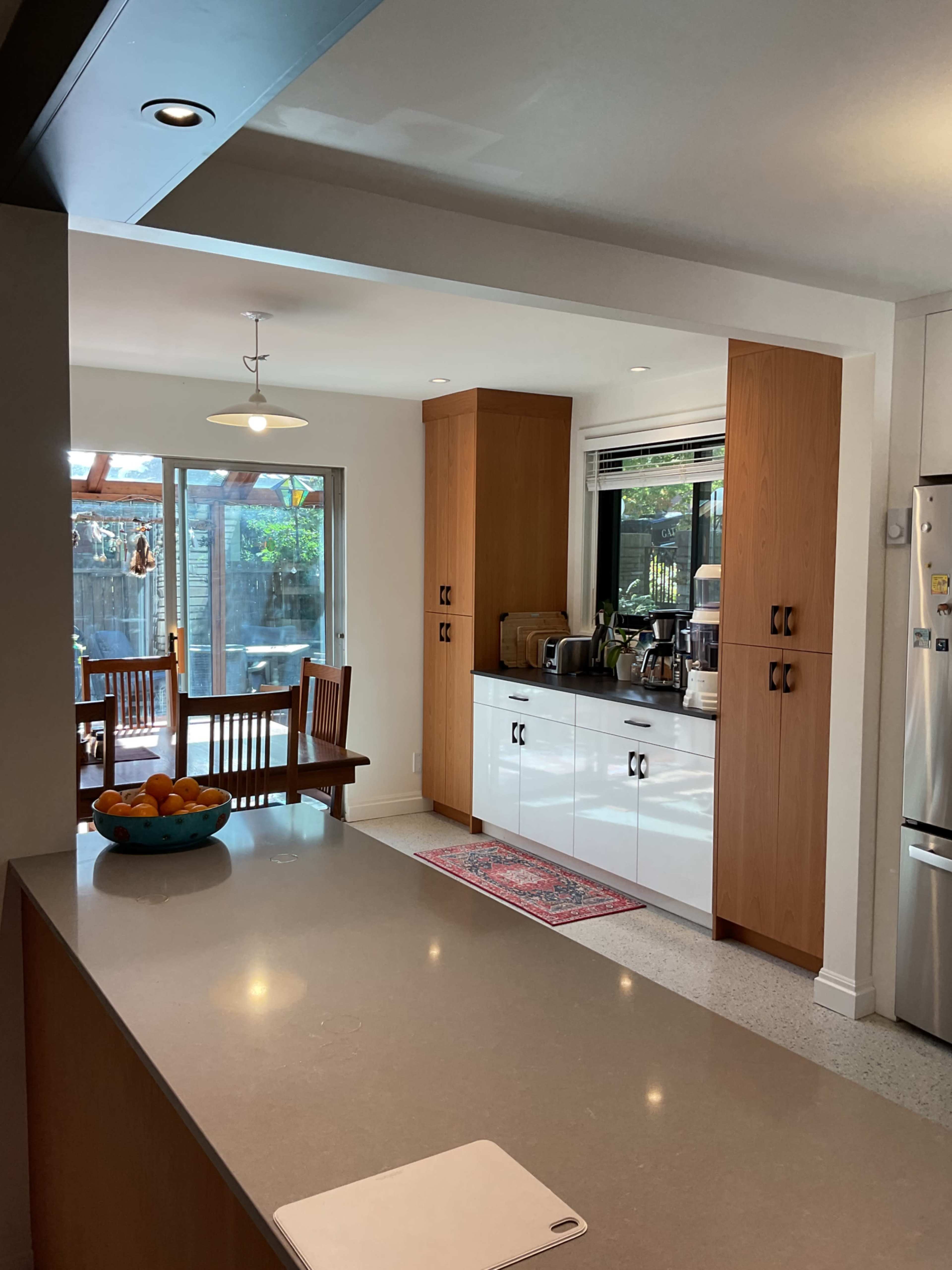 The image shows a modern kitchen with a central island, wooden cabinetry, stainless steel appliances, and a dining area visible in the background.