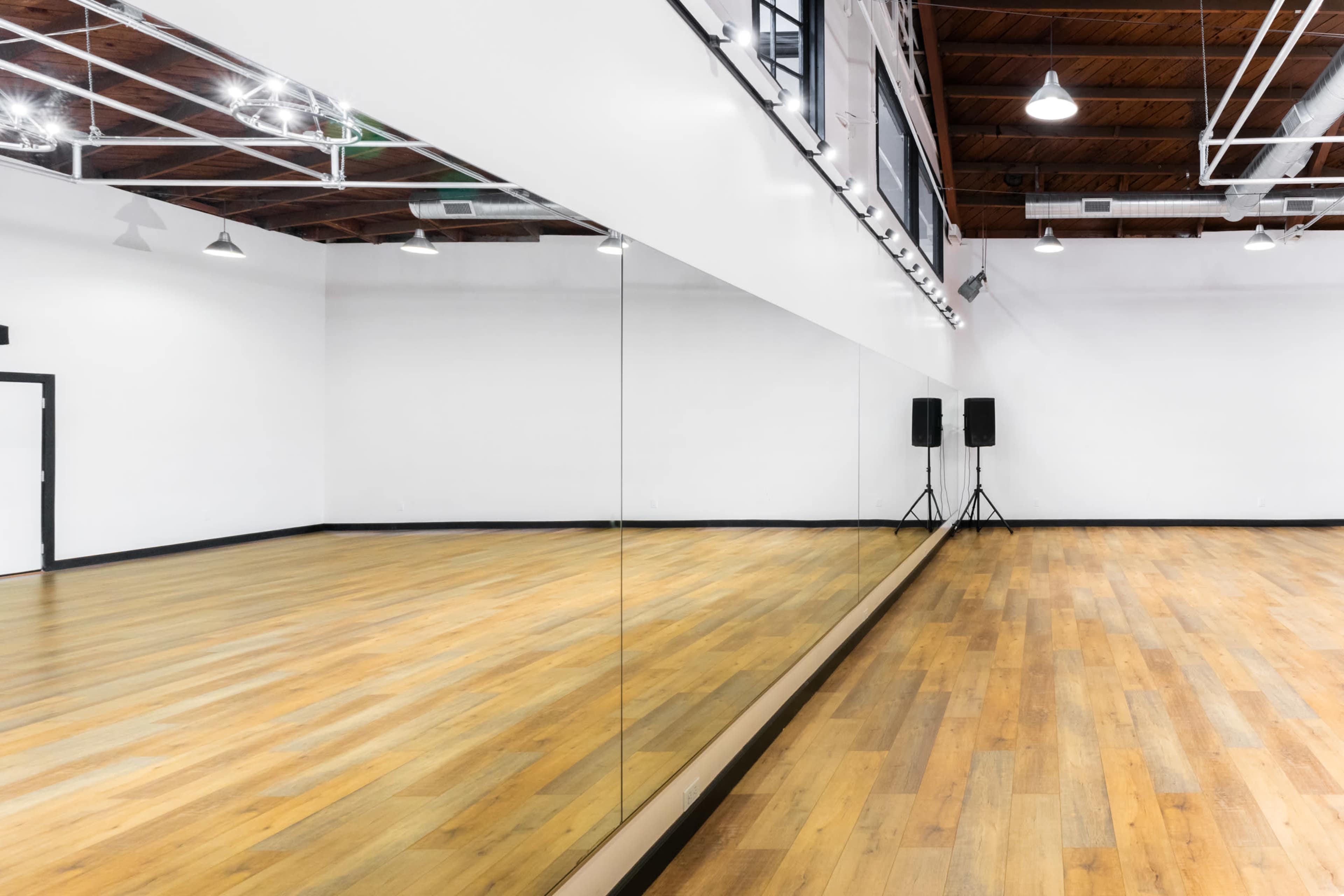 A spacious dance studio with hardwood flooring, white walls, and a large mirror along one side.