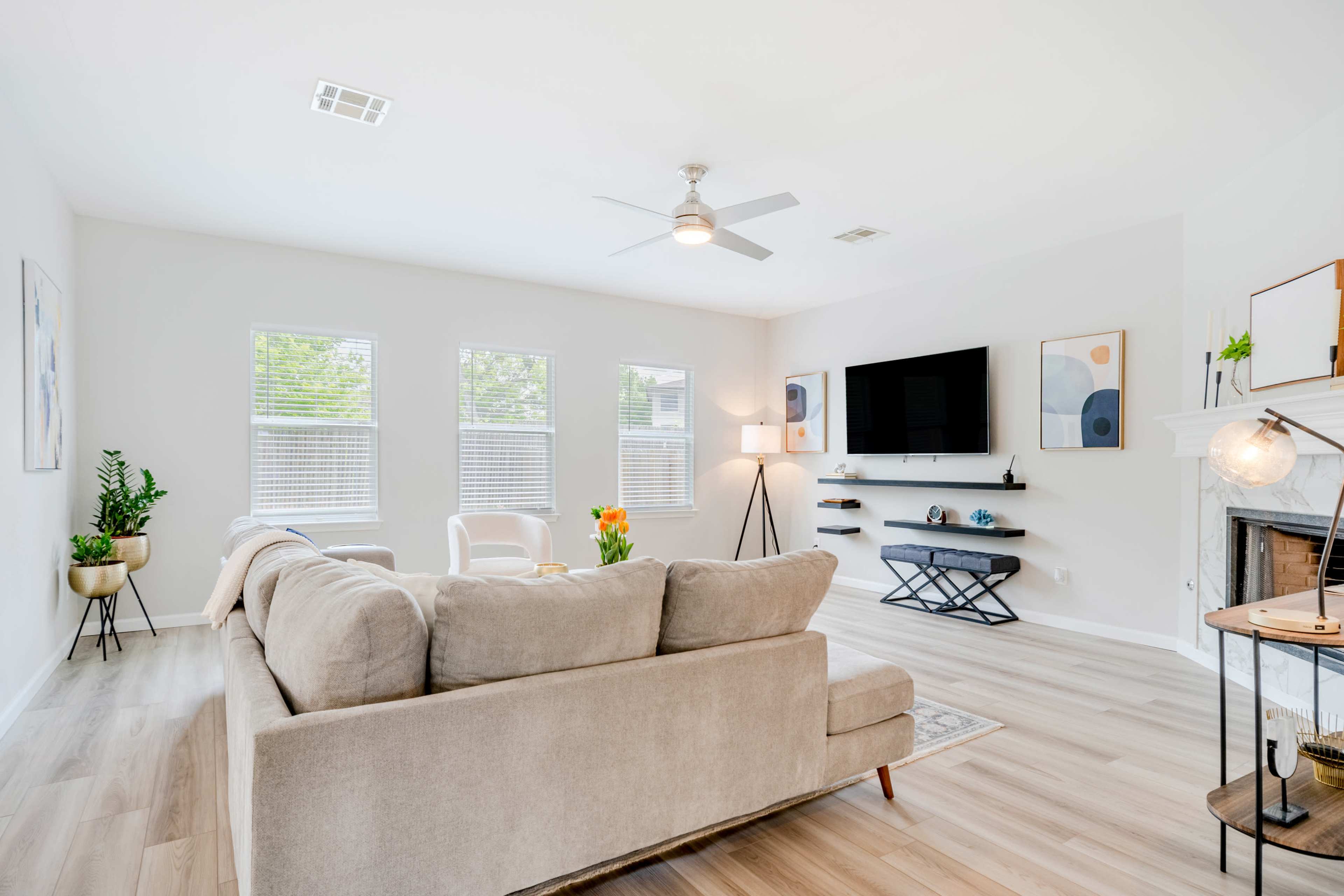 A spacious living room features a light-colored sectional sofa, a mounted television, and large windows allowing natural light to fill the space.