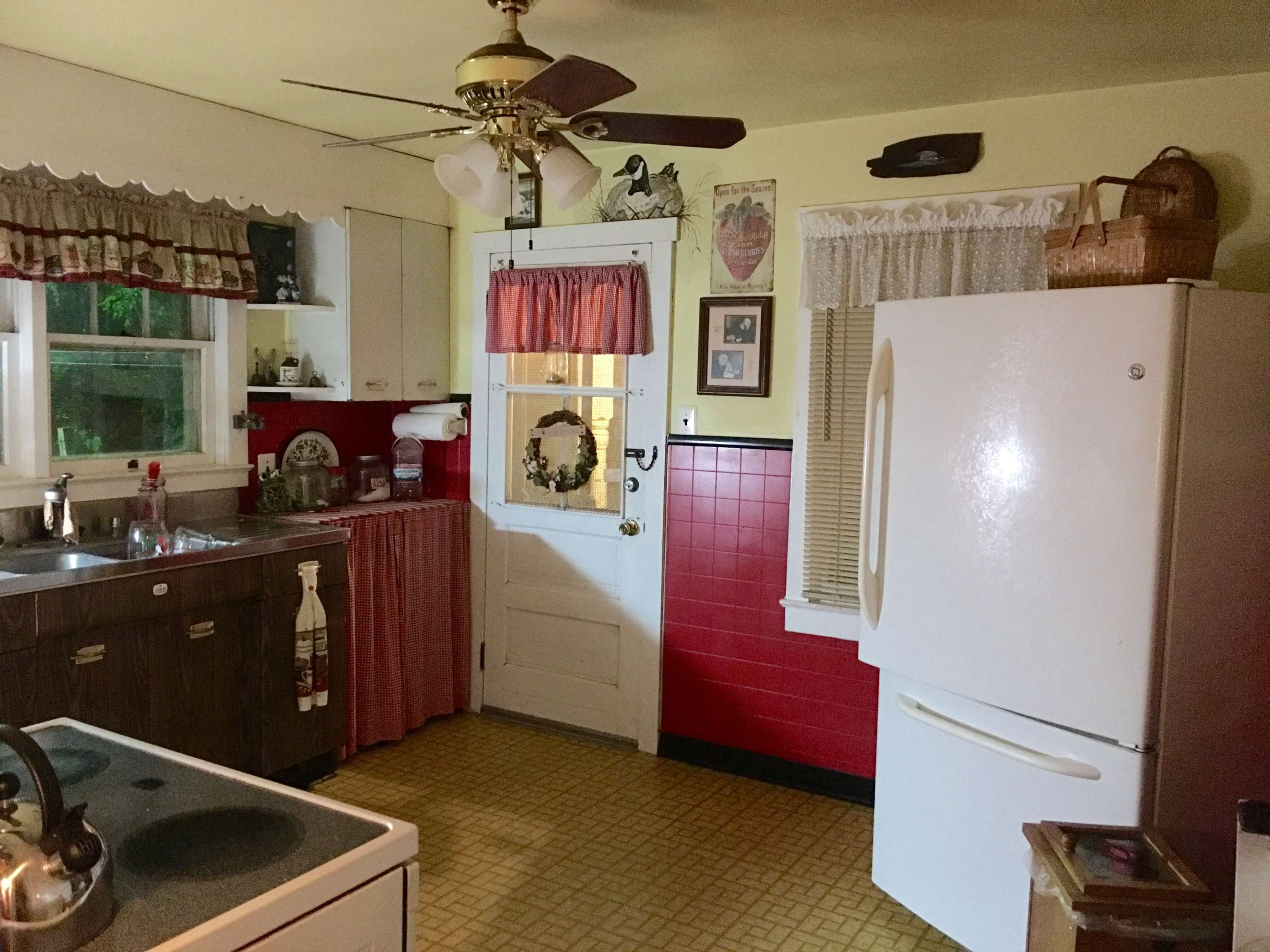 A kitchen with wooden cabinets, a white refrigerator, a red wall, and a door leading outside.