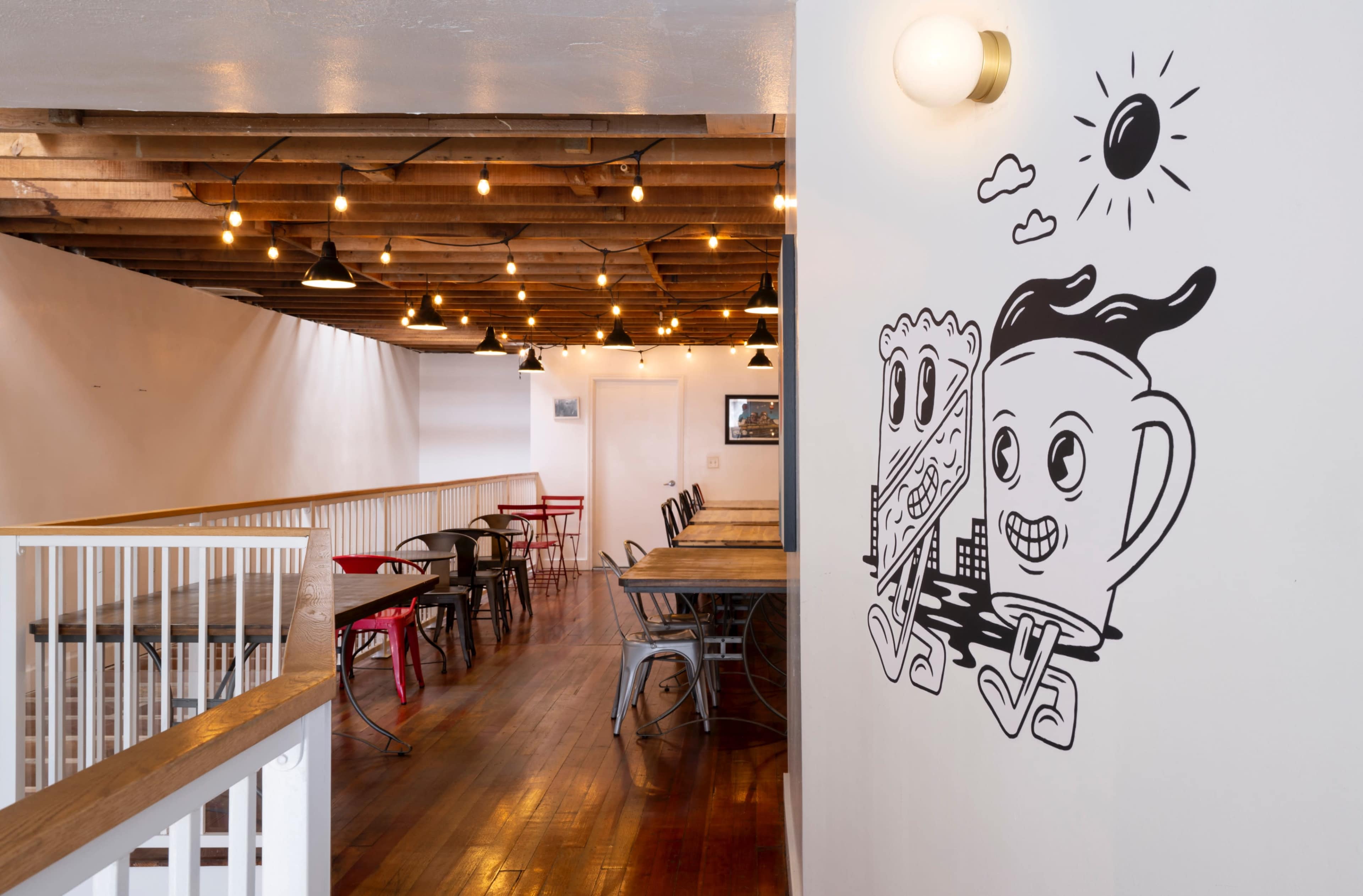 A brightly lit café interior with wooden beams, string lights, and a mural of cartoon characters on the wall.