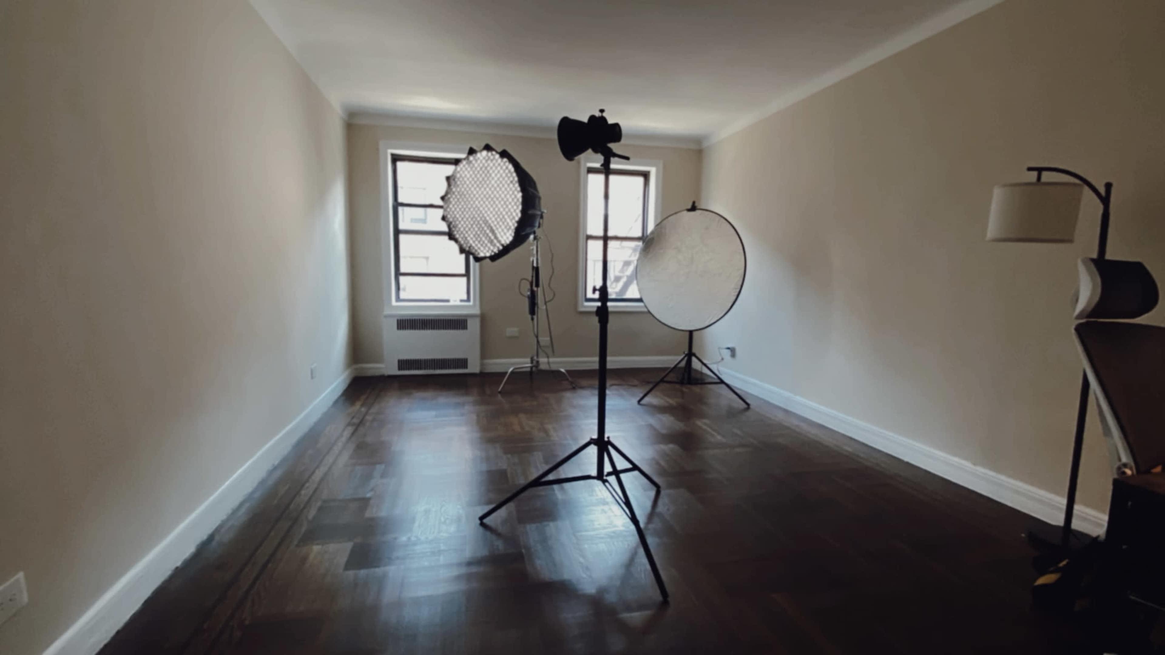 An empty room with hardwood floors is set up for a photo shoot, featuring light stands and softboxes.