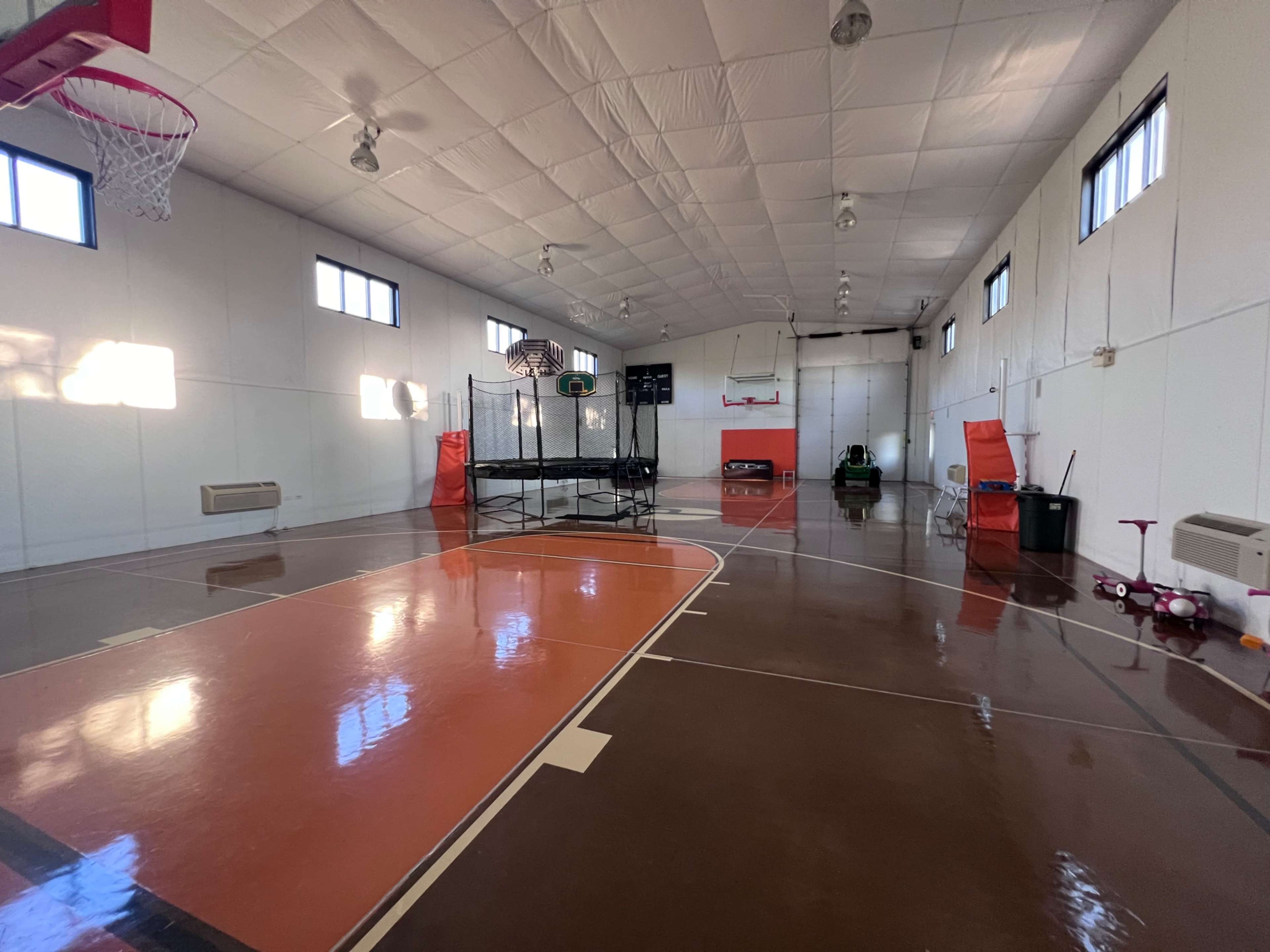 The image shows an indoor gymnasium with basketball hoops, polished floors, and various sports equipment.