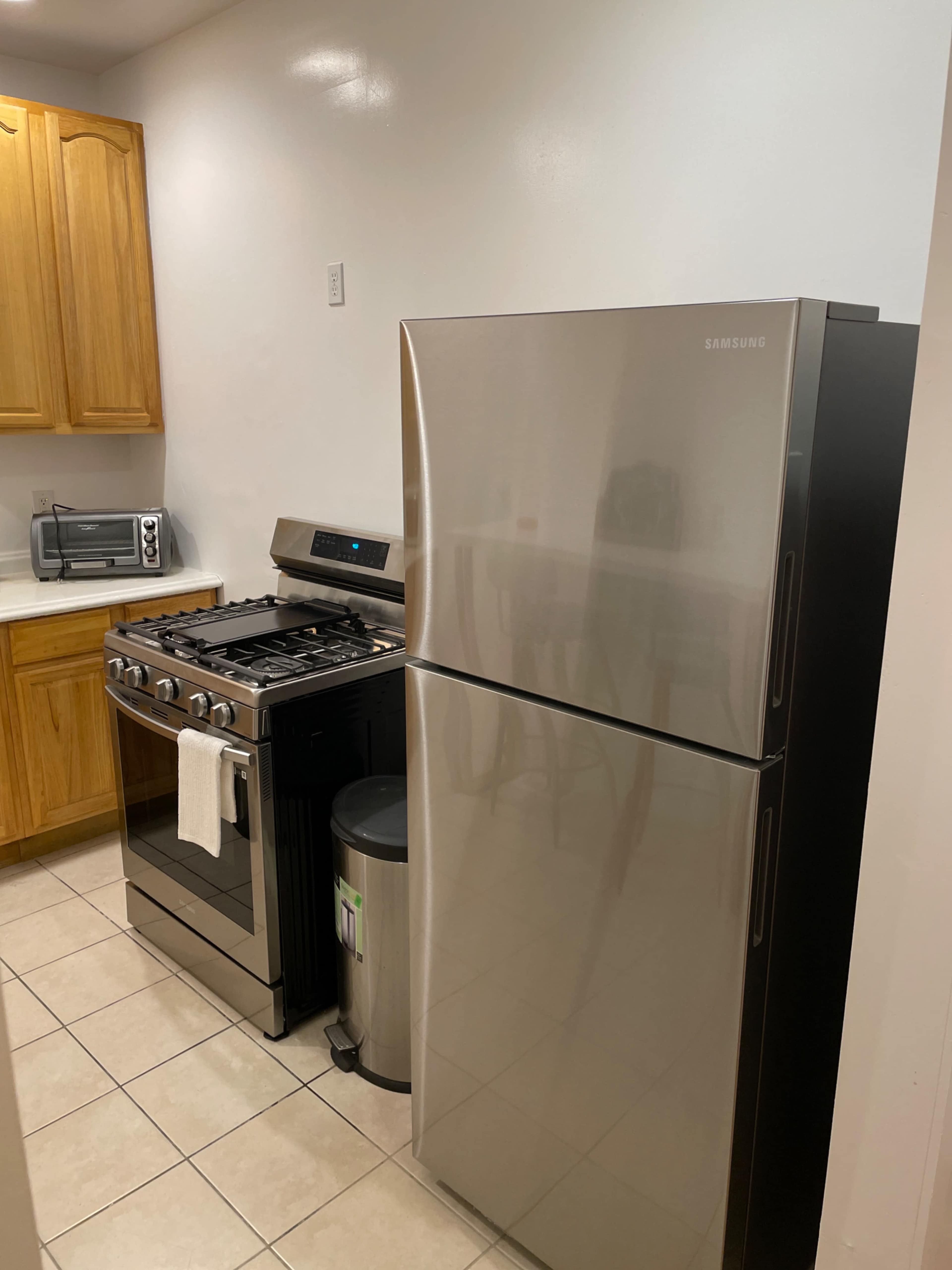 A kitchen with a stainless steel refrigerator next to a stainless steel gas stove, with wooden cabinets above and a microwave on the counter.