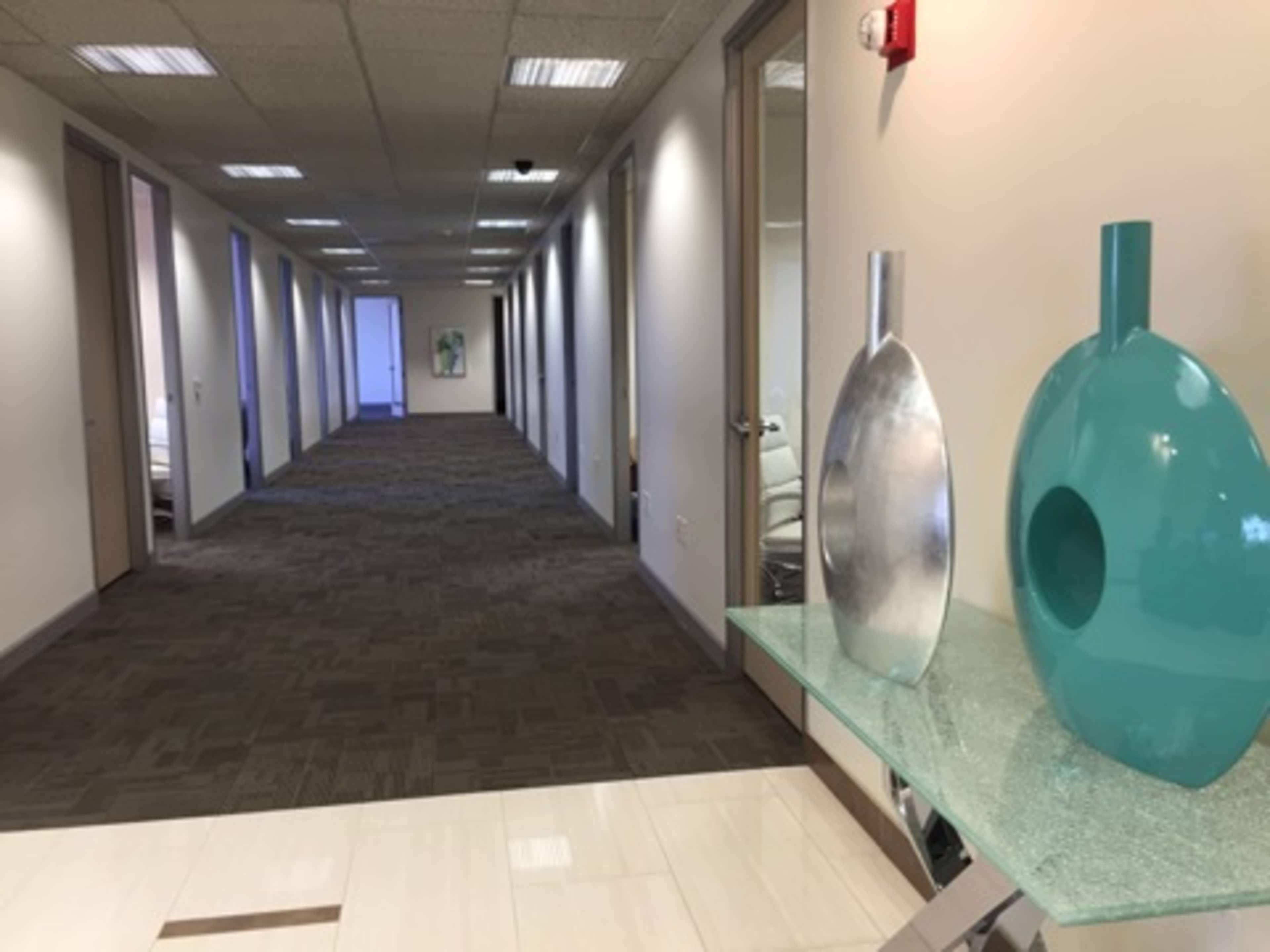 A long hallway in an office building with doorways on either side and two decorative vases on a console table at the entrance.