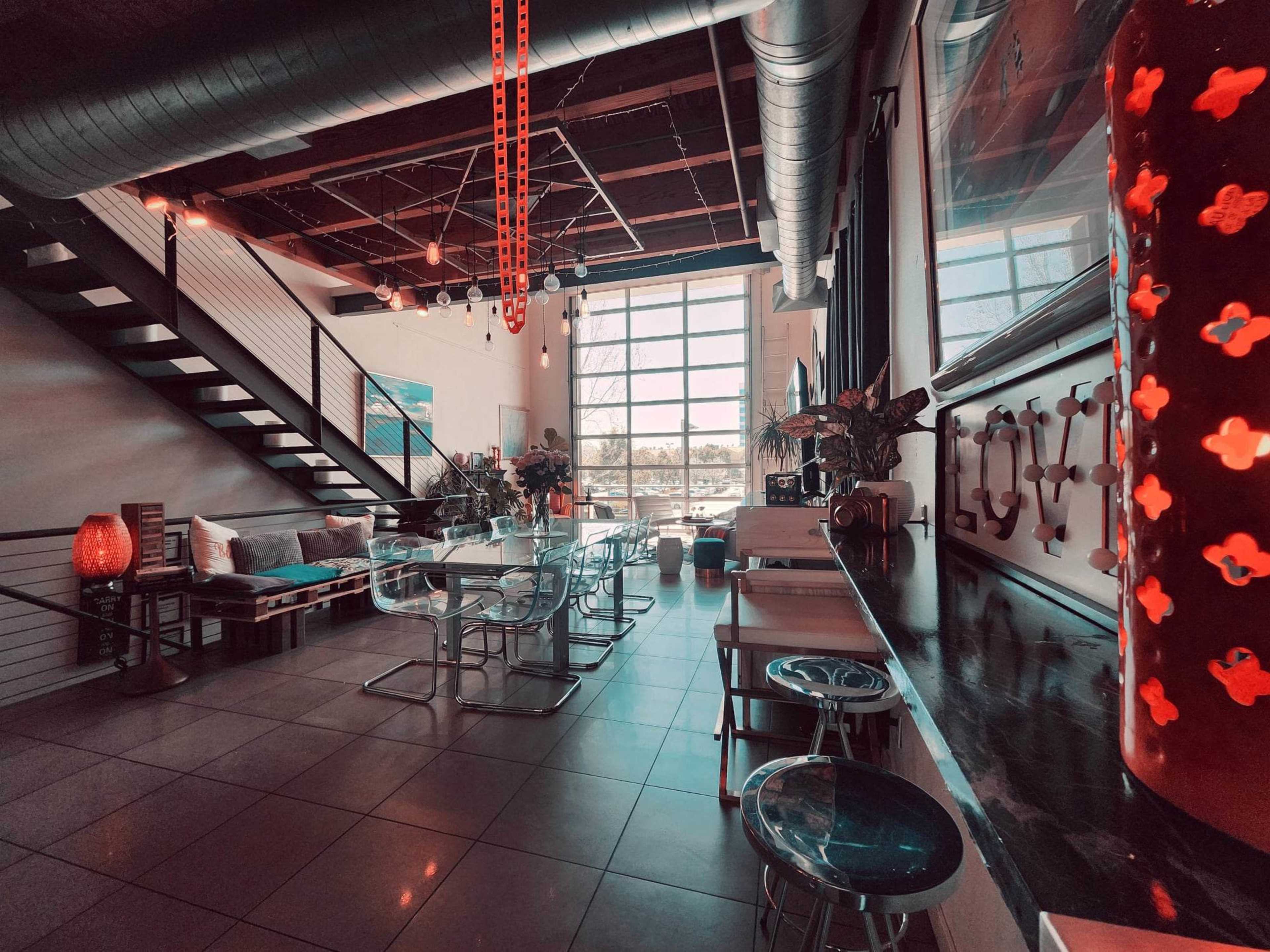 A modern interior space with a dining area featuring glass furniture, a staircase, large windows, and decorative elements.