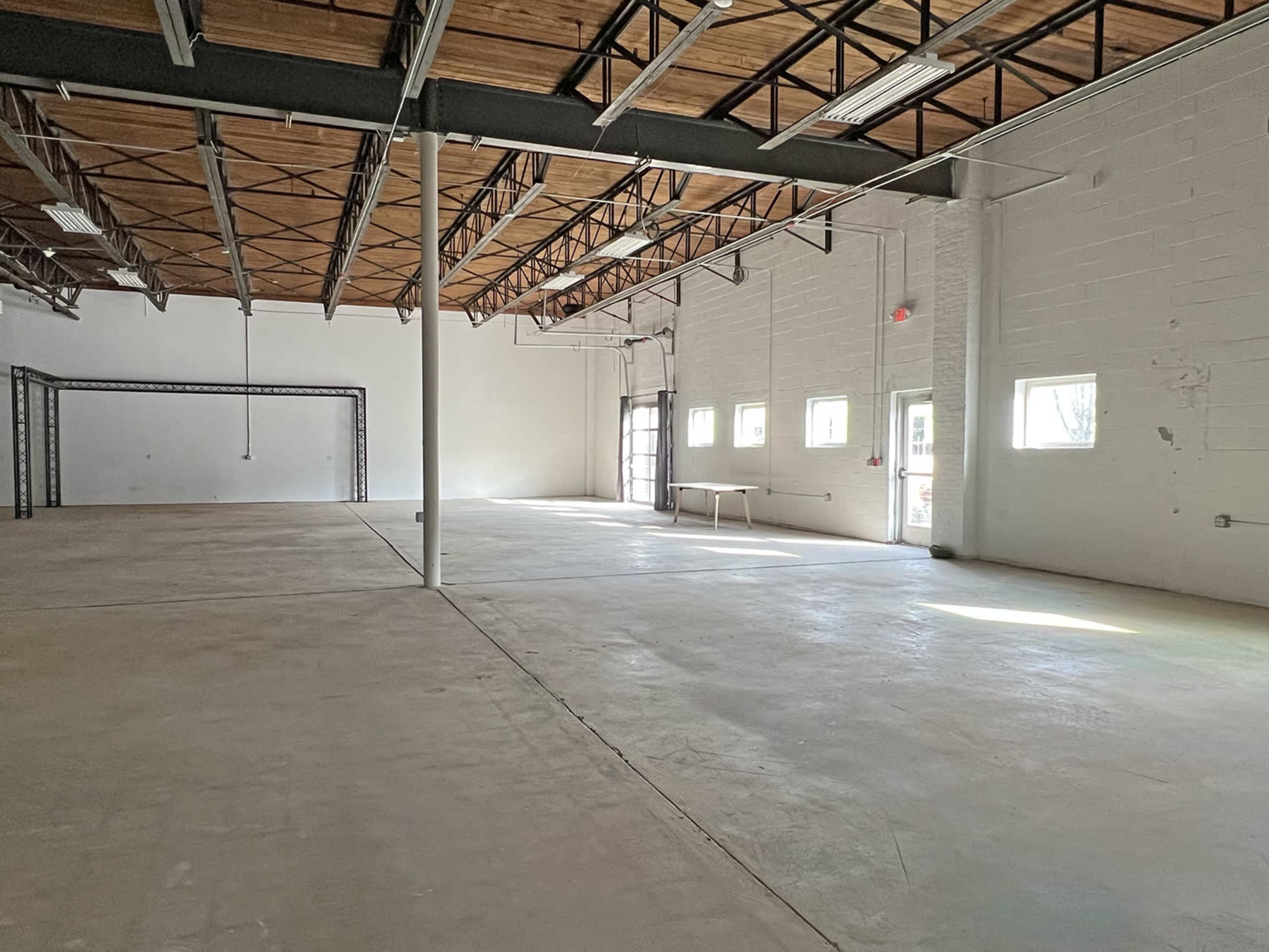 A large, empty industrial space with high ceilings, concrete flooring, and several windows along the walls.