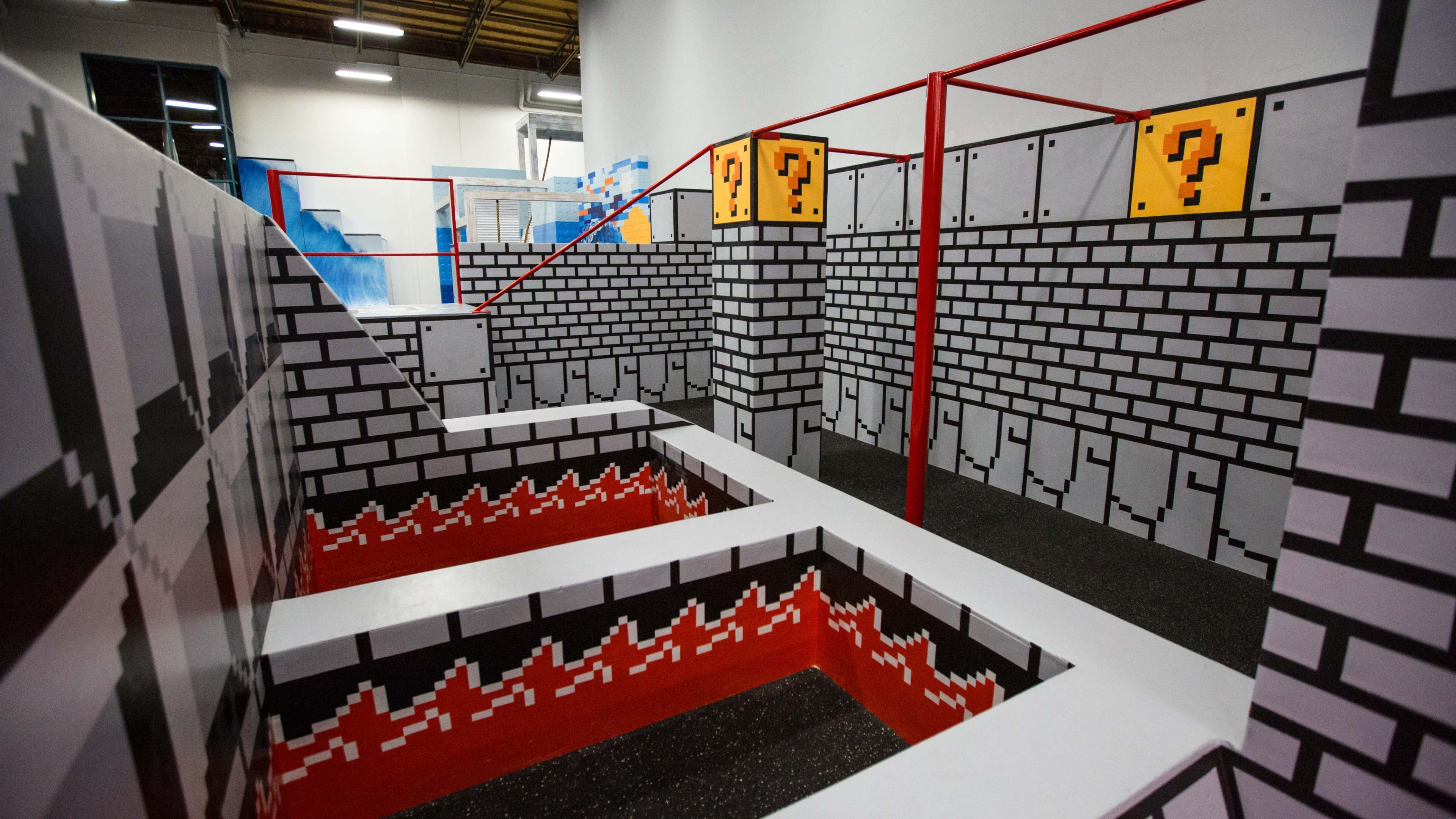 A colorful indoor obstacle course designed to resemble a video game level, featuring brick walls, question mark blocks, and a multi-level layout with red accents.