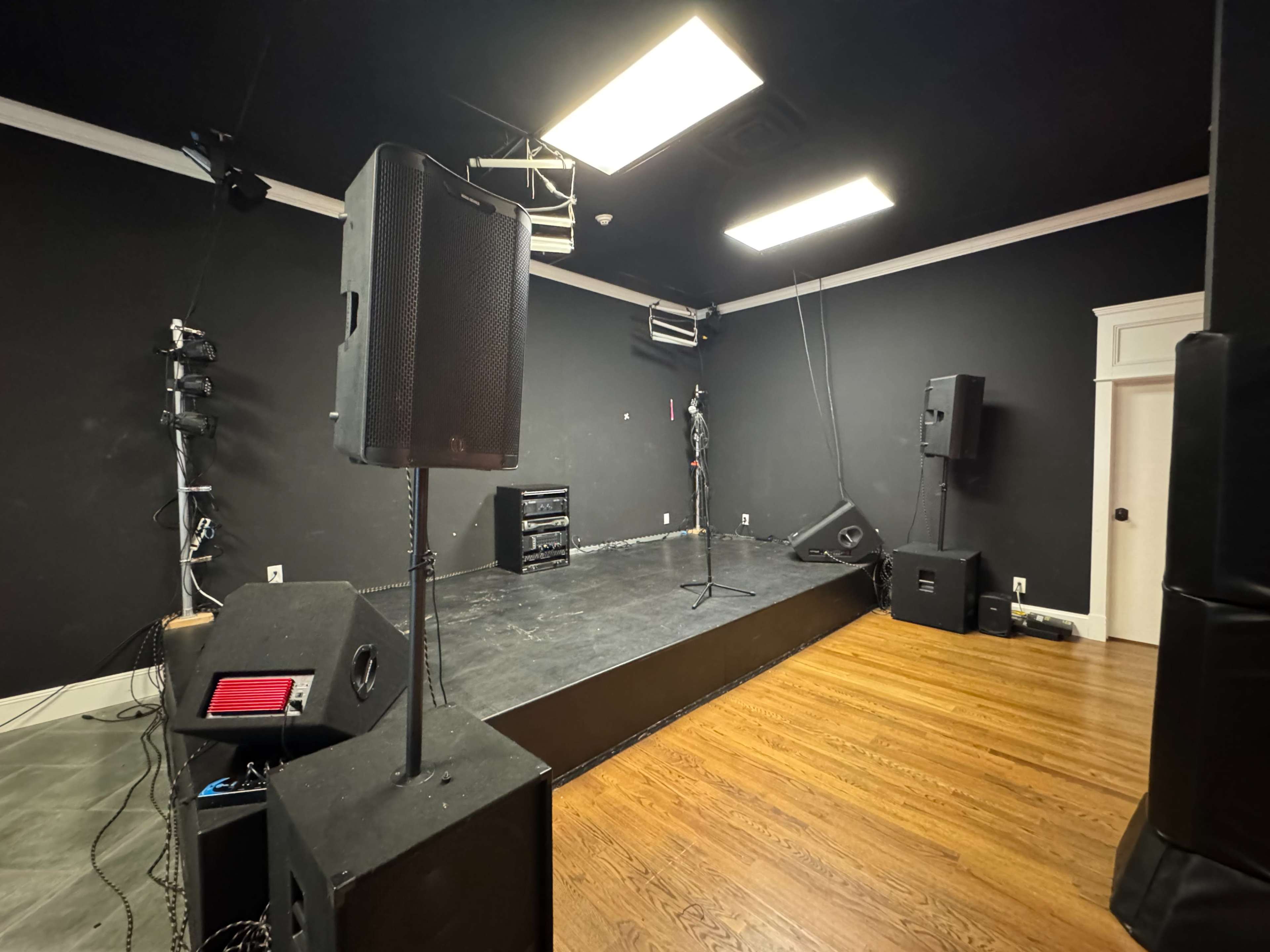 The image shows a small stage area with a microphone, two large speakers on either side, and a dark black wall behind.