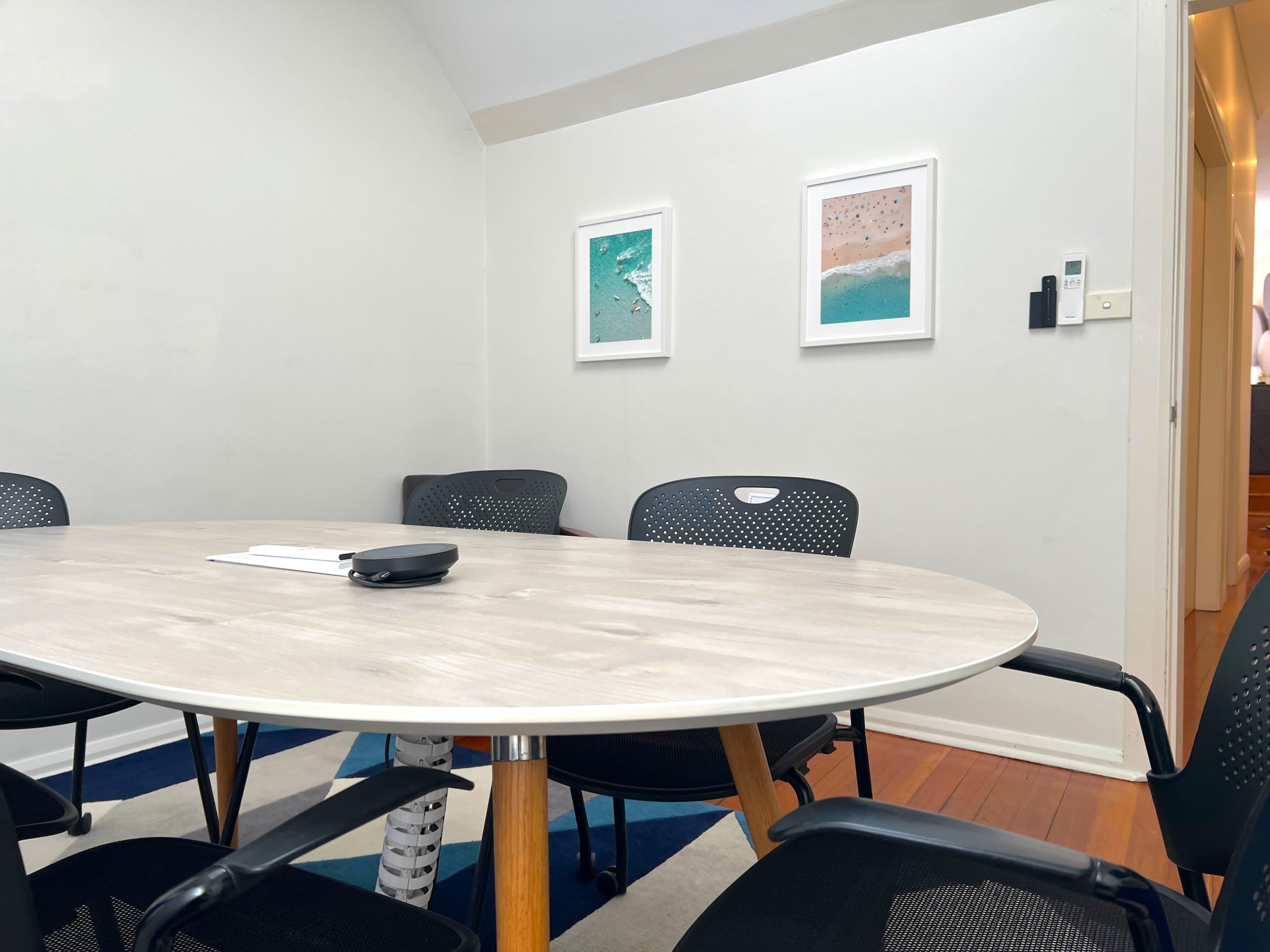 A round table surrounded by black chairs sits in a small conference room, with framed artwork on the wall.