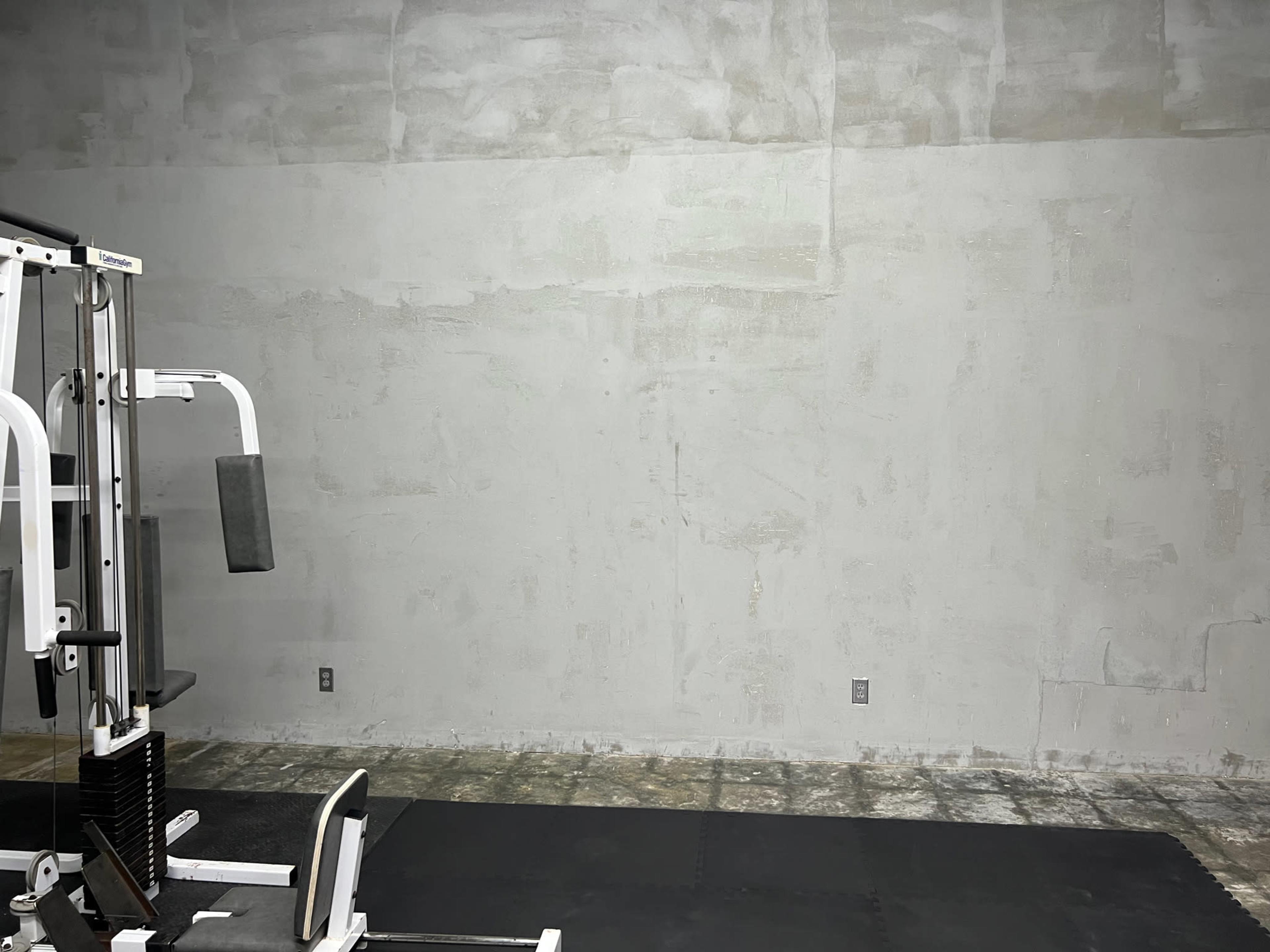 A gym area featuring a weight machine and a gray, unfinished wall.