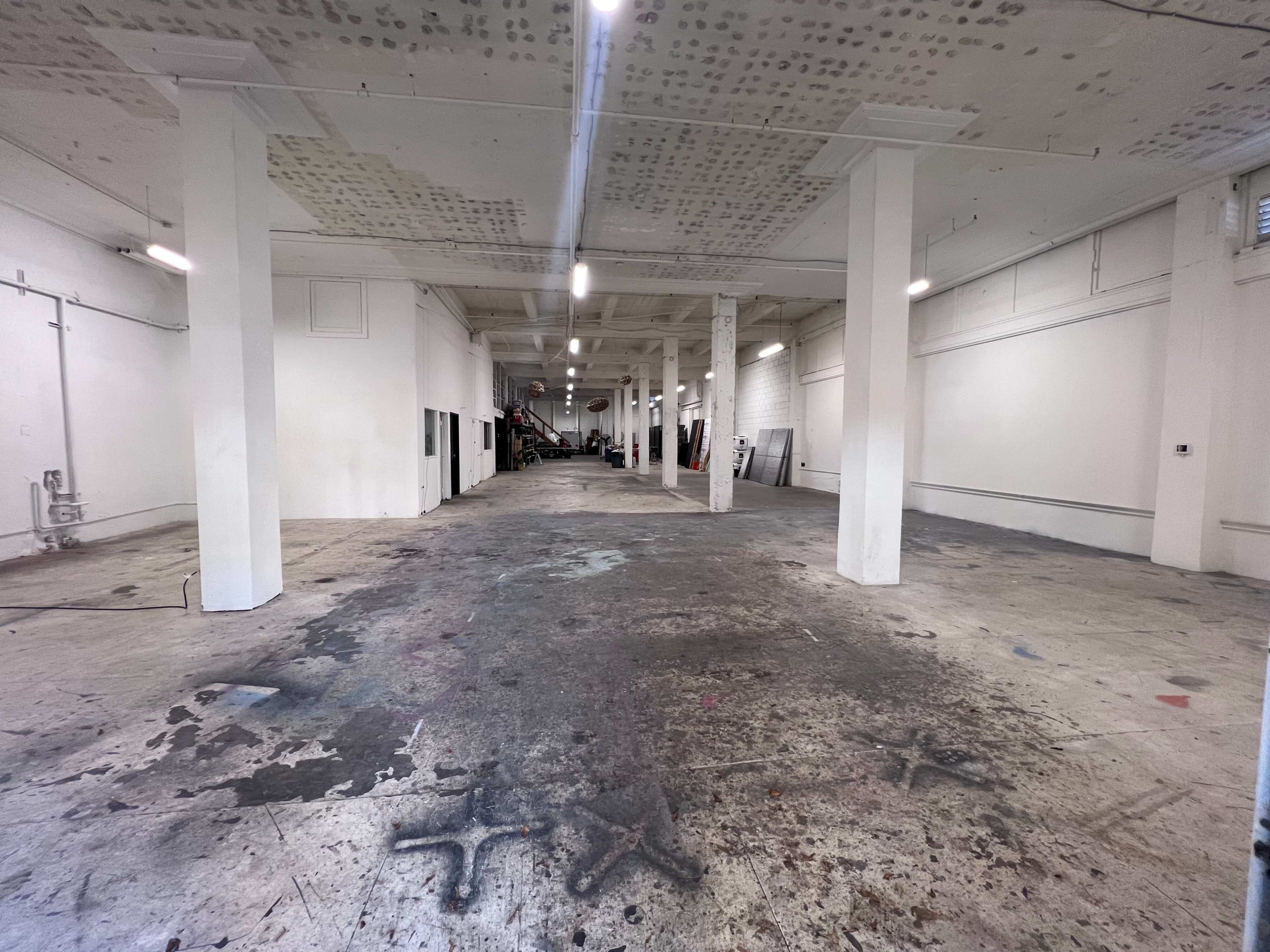 A large, empty industrial space with concrete floors and white walls, featuring several columns supporting the ceiling.