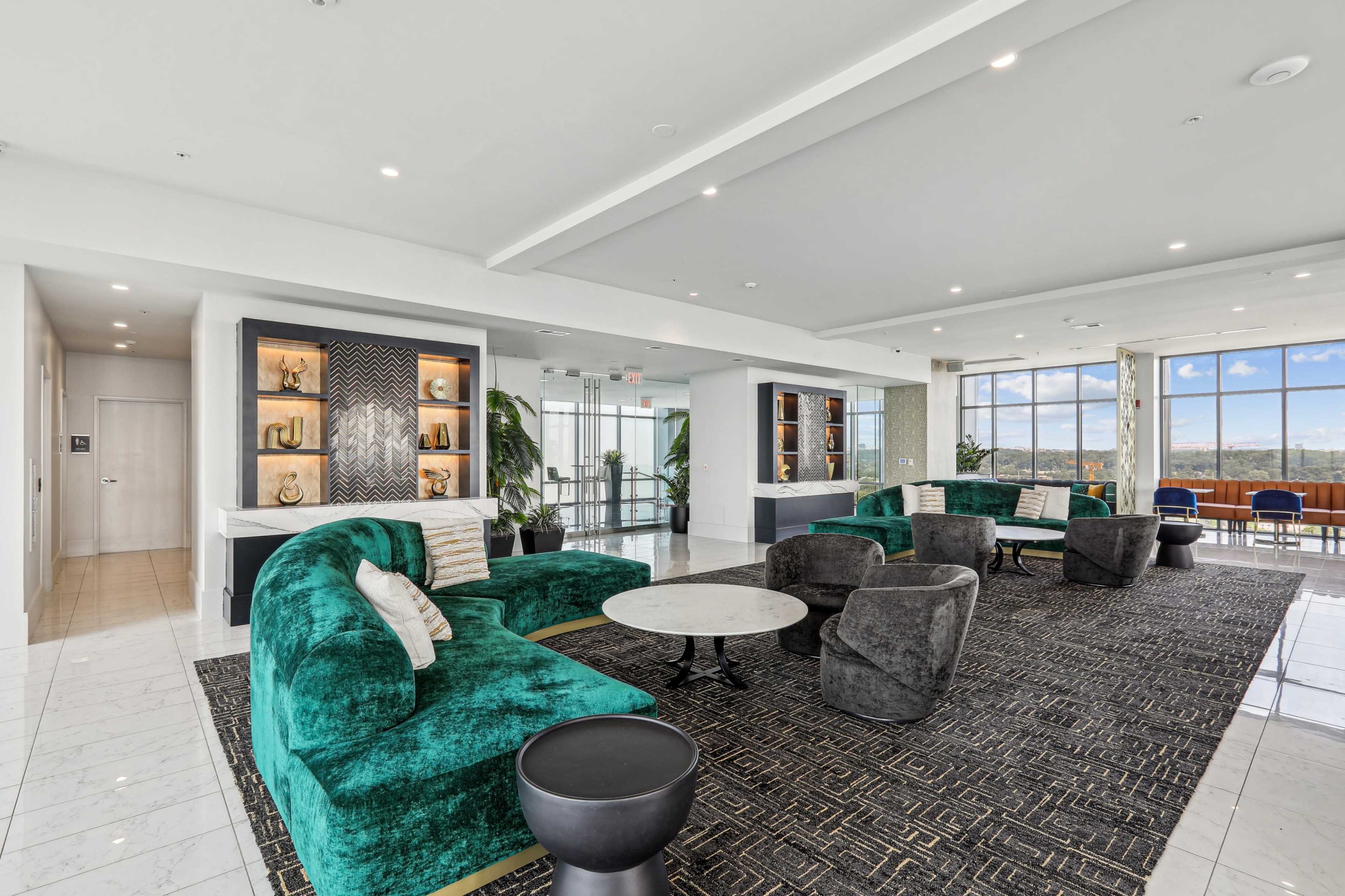 A modern lounge area featuring green velvet seating, a round coffee table, and large windows with a view.