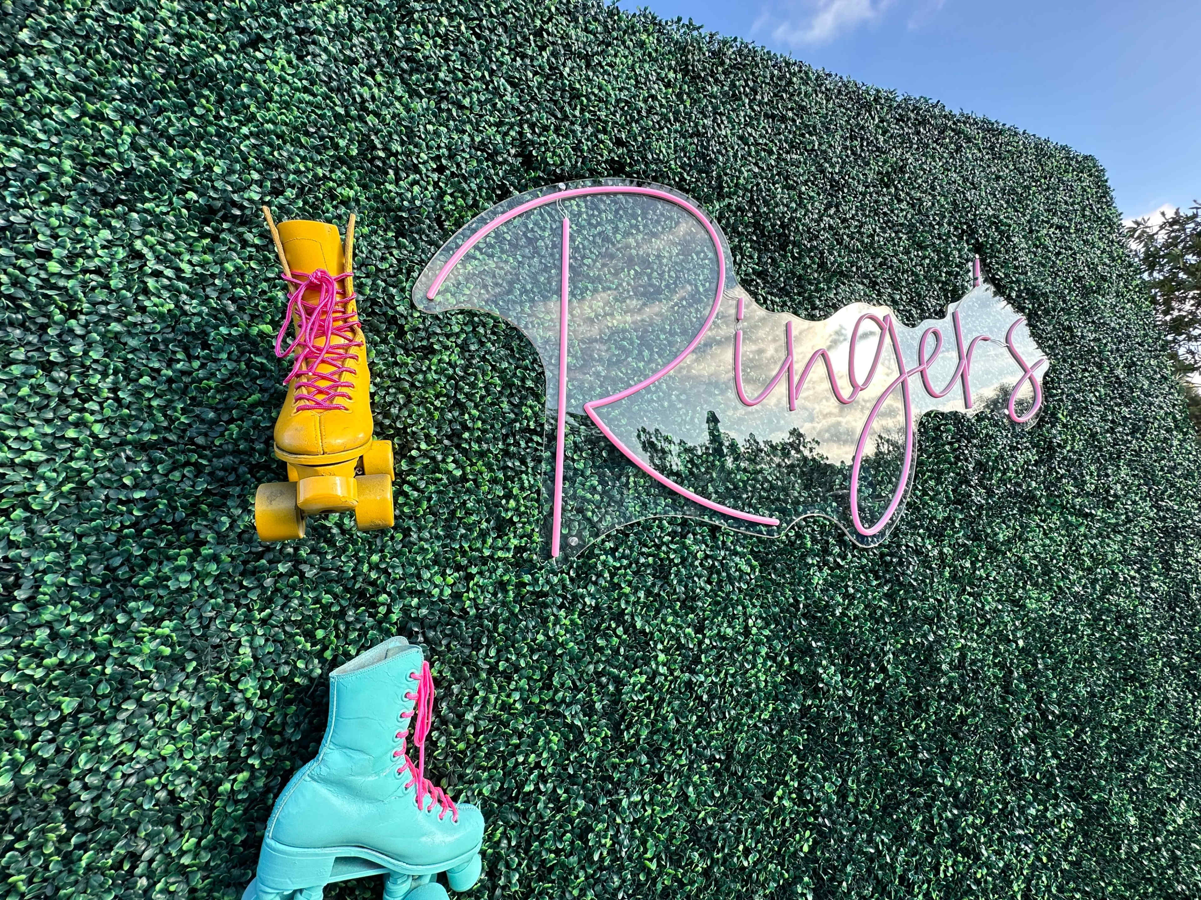 A green wall with the word "Ringer's" in pink lettering, adorned with vibrant yellow and teal roller skates attached to the surface.